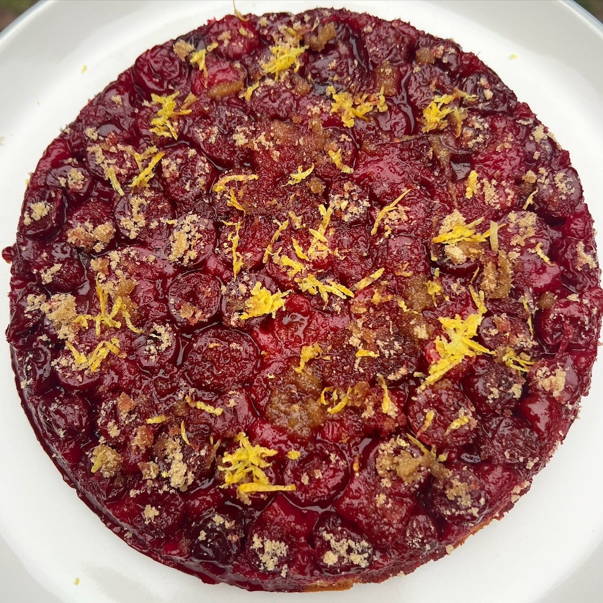 Upsidedown Morello cherry cake topped with lemon zest, served on a white plate.