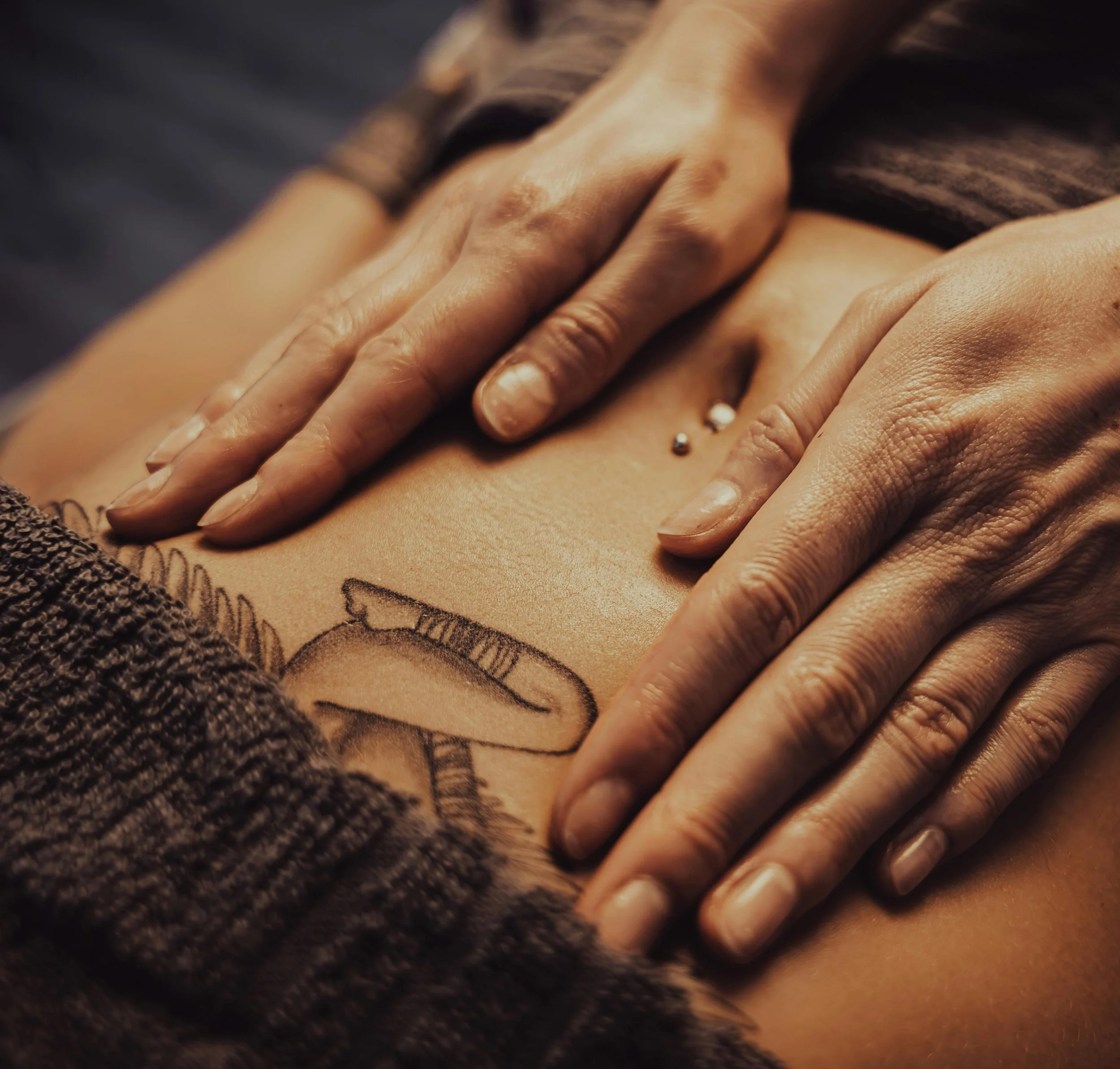 Nahaufnahme eines Tattoos eines Vogel auf einer menschlichen Haut, mit Händen, die das Tattoo berühren, und einem Bauchnabelpiercing.