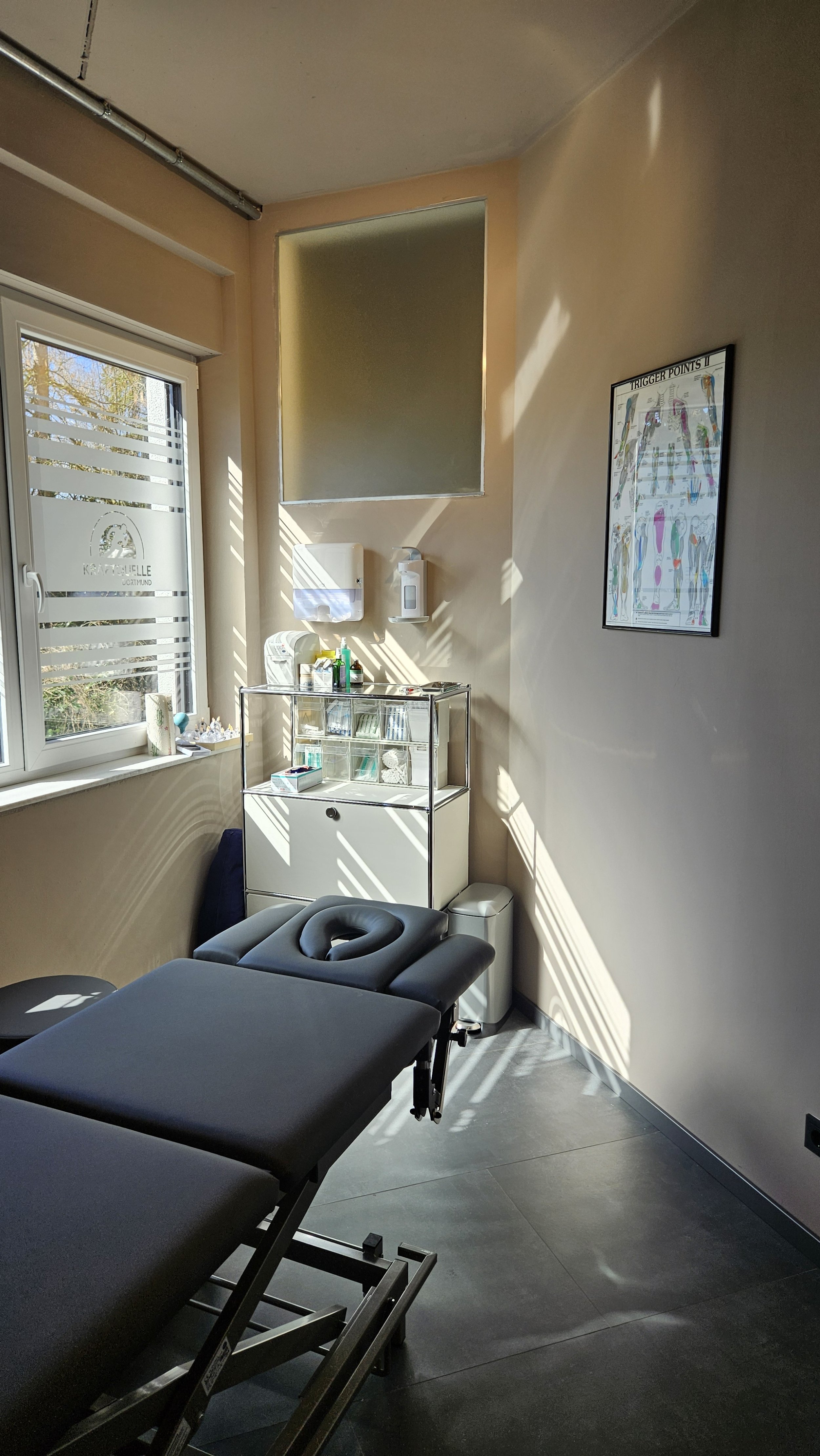 Behandlungsraum in einer Praxis mit Behandlungsliege, Fenster und medizinischen Utensilien.