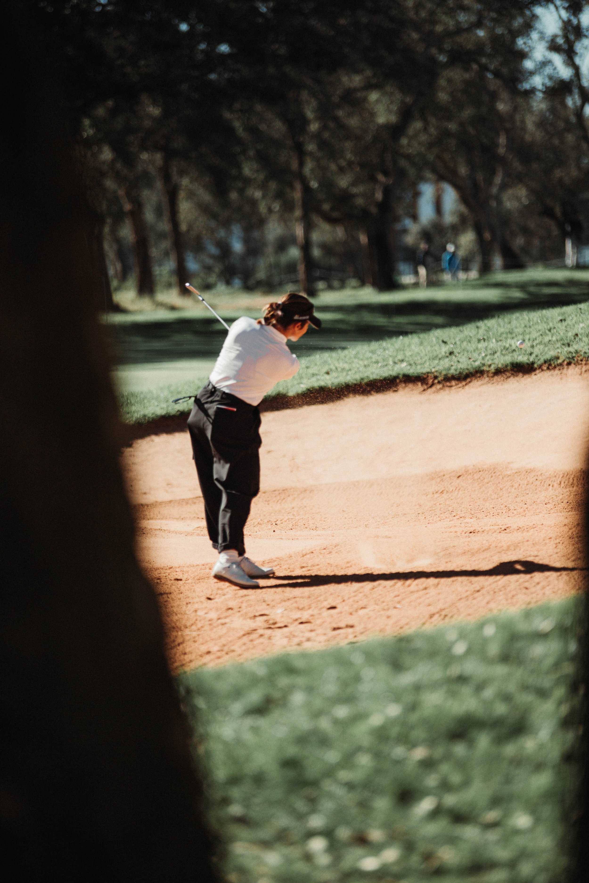 Ana Pelaez Triviño jugando golf en un búnker de arena, rodeada de árboles en un campo de golf.