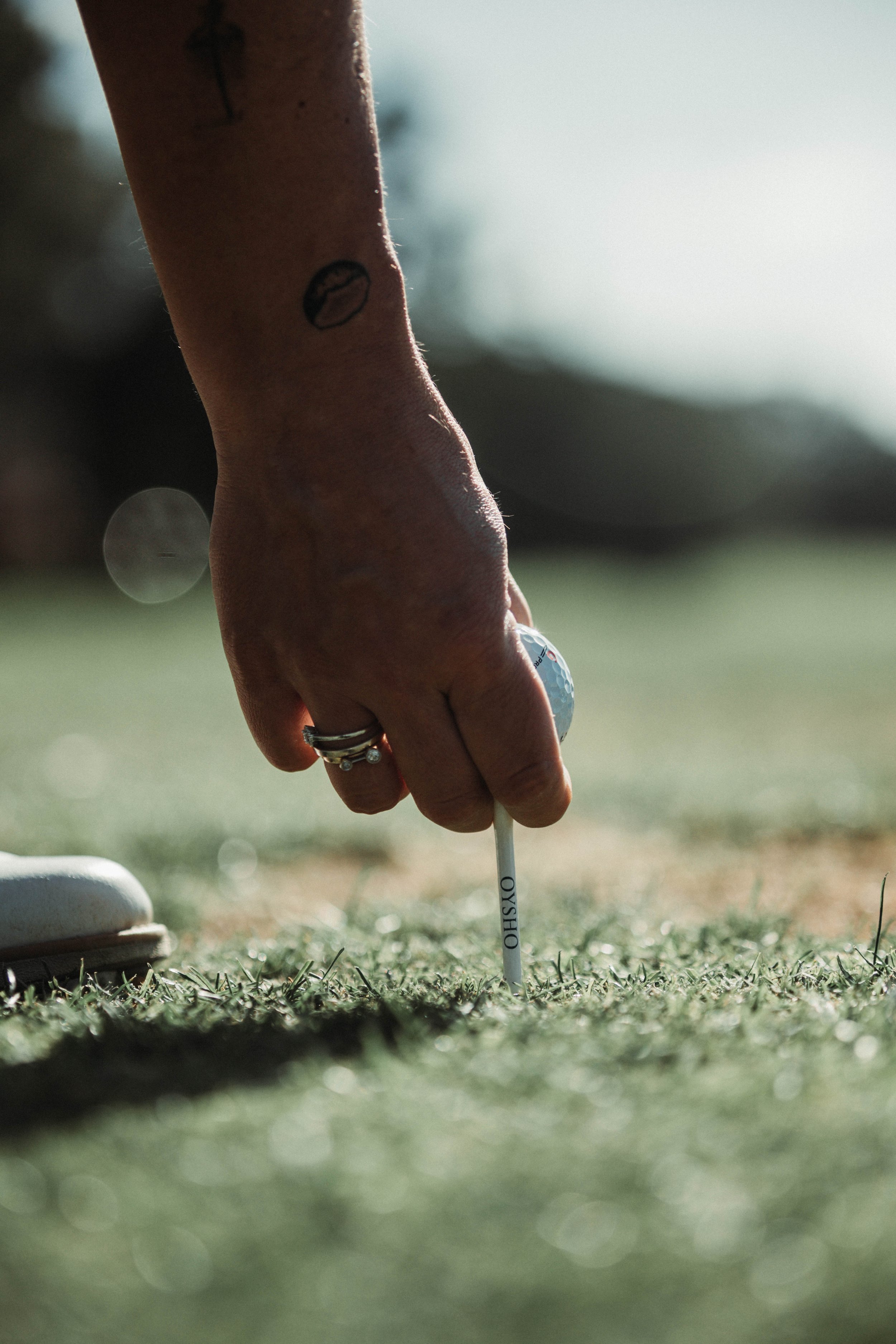 Mano colocando una pelota de golf sobre un tee en el césped.