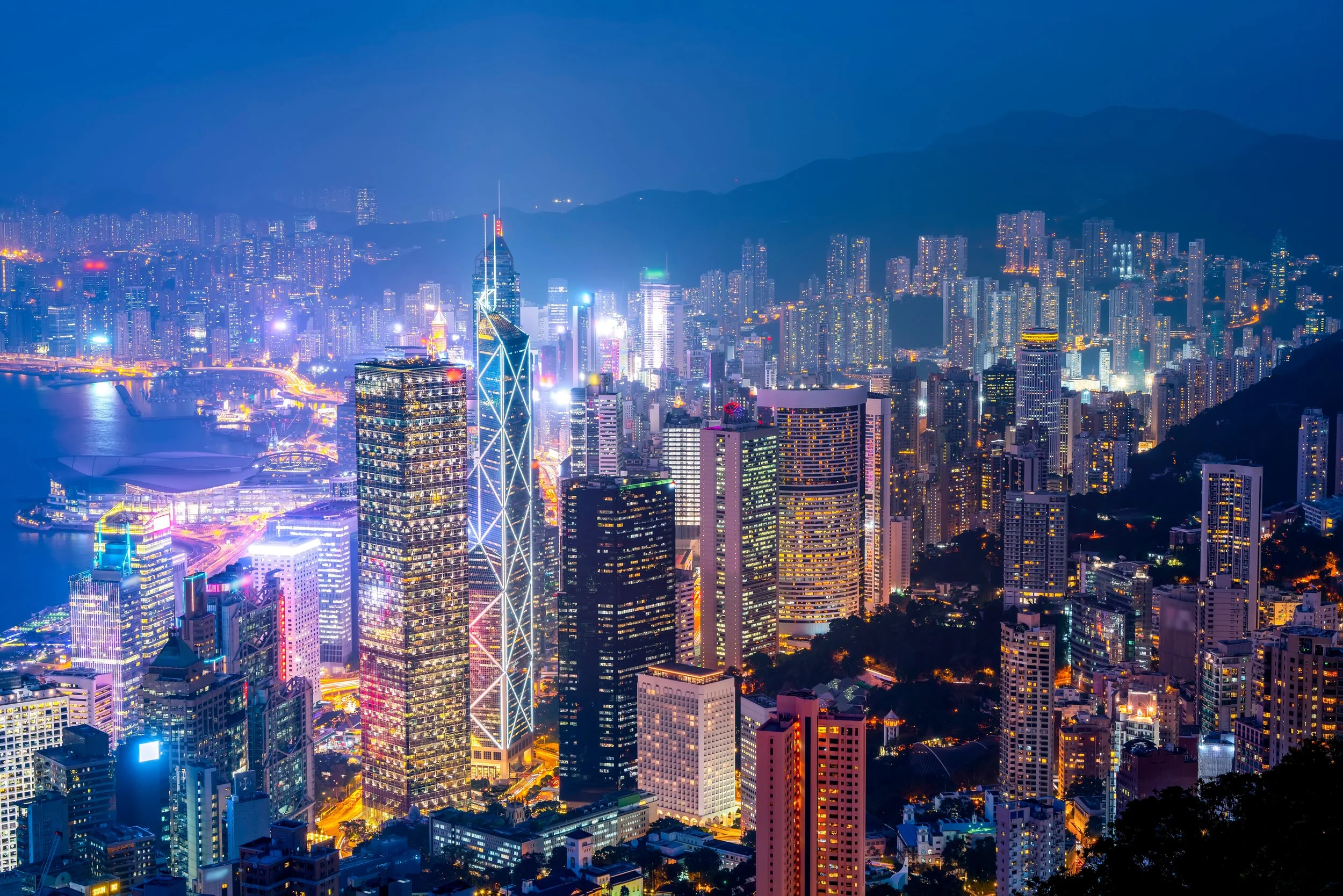 A cityscape at night with illuminated skyscrapers and buildings, a river with bridges, and mountains in the background.
Hong Kong, Hong Kong investor, US investment, Capital investment, invest HK, Miami invest