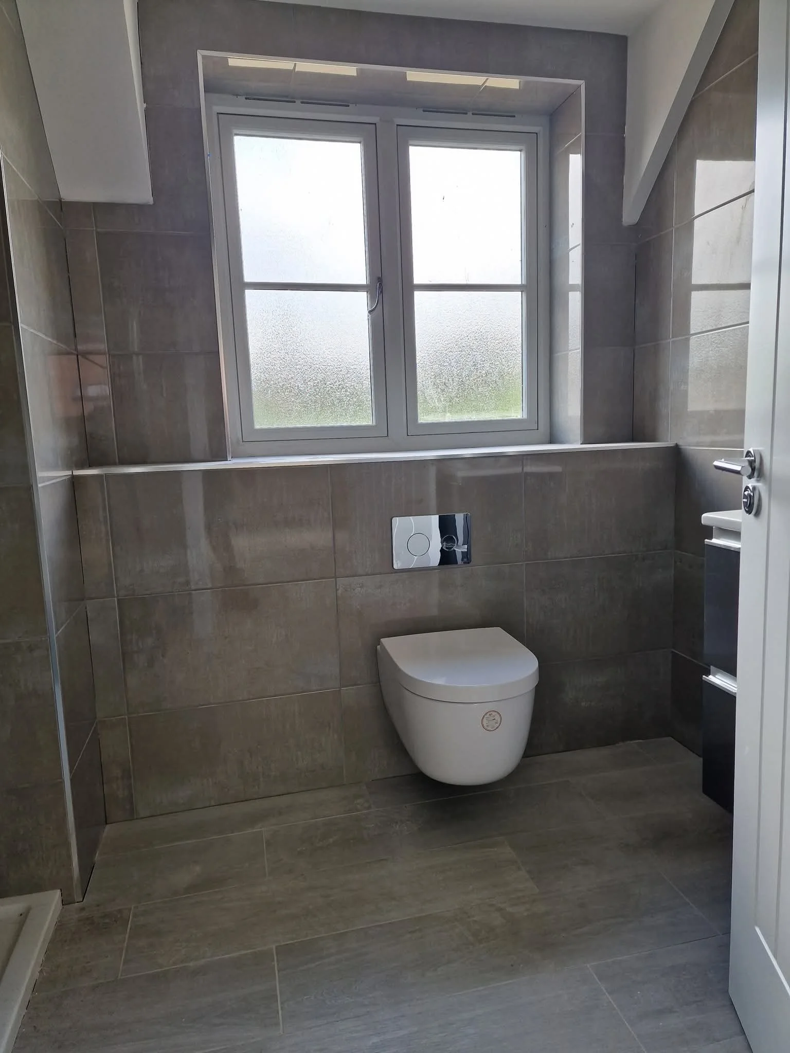 A modern bathroom with a wall-mounted toilet below a frosted window and tan tiles. modern ceramic tiles Porcelanosa Millbrook by tile infinity romsey southampton.