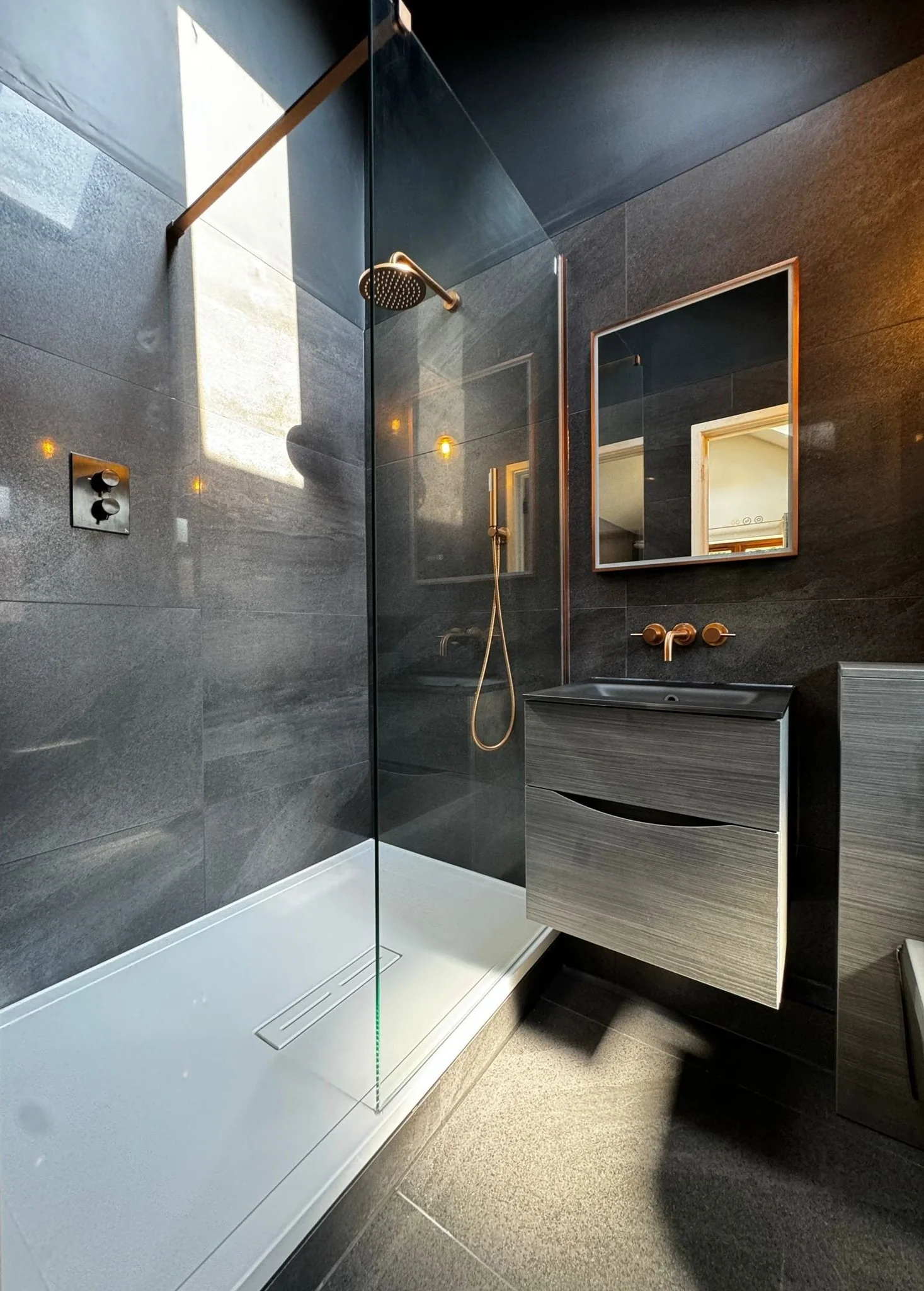 floor tiling services for a Modern bathroom tiling project by tile infinity southampton, with glass shower enclosure, black tile walls, and a sleek vanity with a mirror.