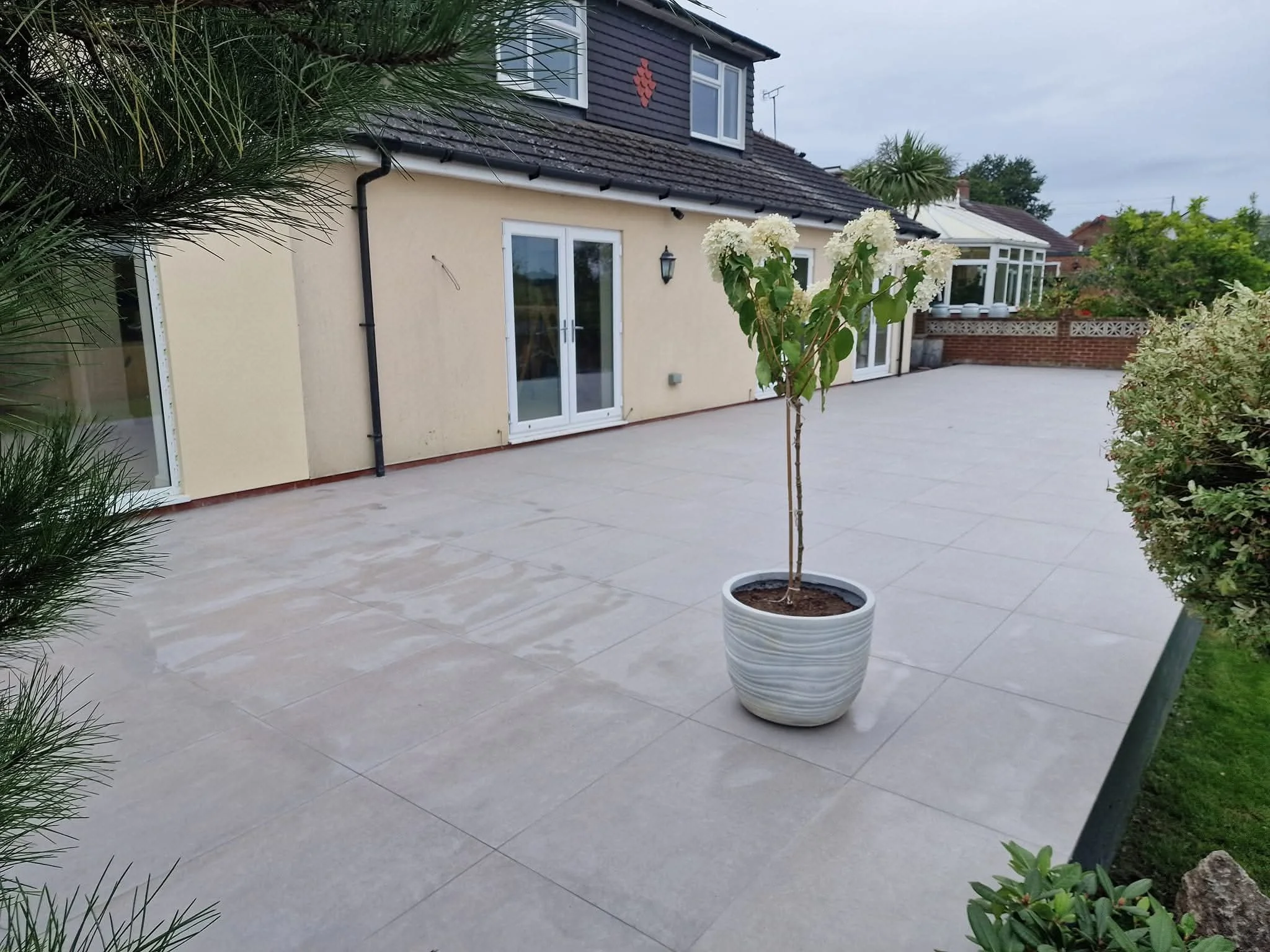 floor tiling services hedge end, add flair to this Modern patio with tile flooring and a potted plant in front of a beige house with sliding glass doors. outdoor porcelain tile infinity hedge end southampton