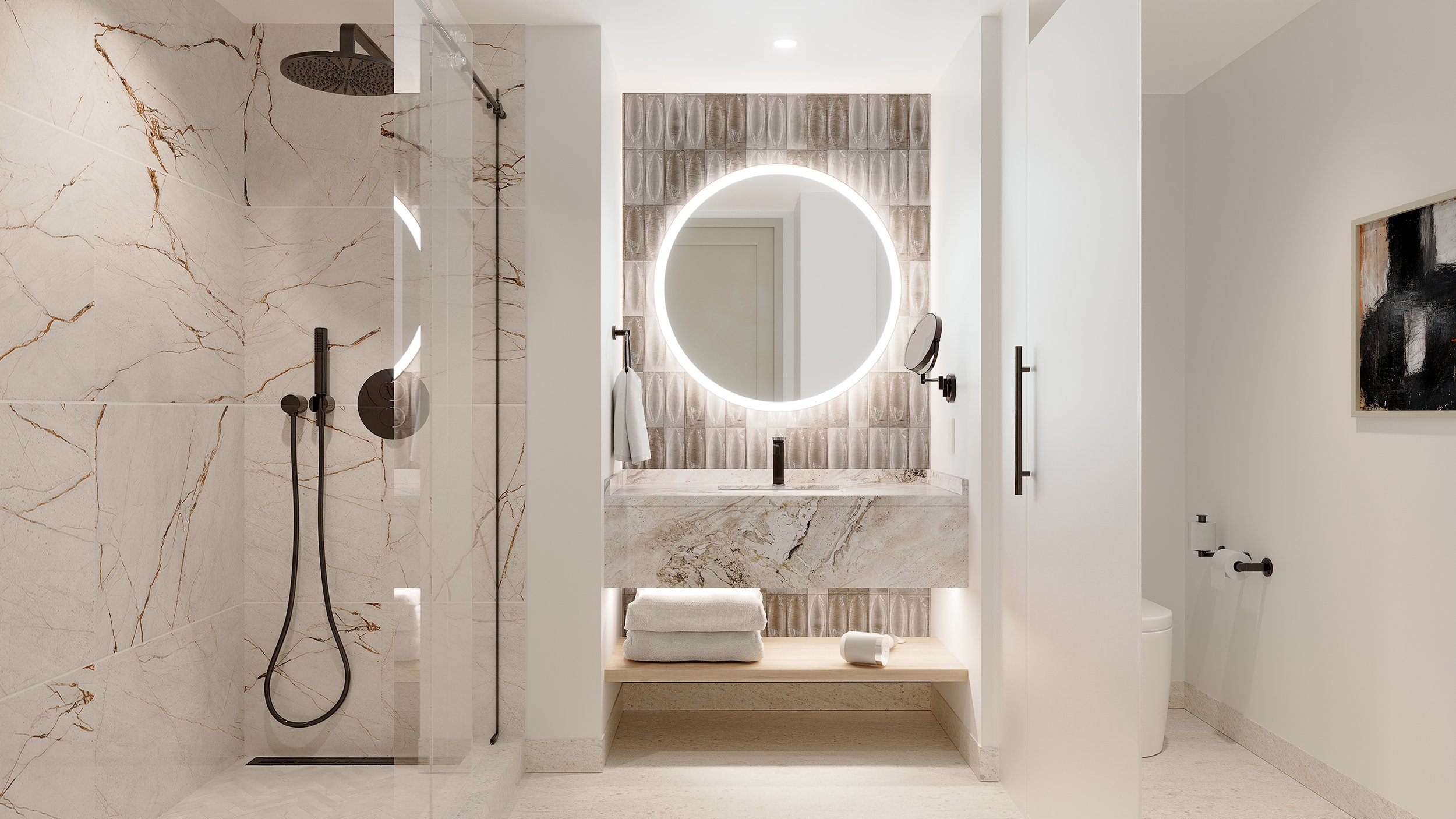 Modern bathroom with a walk-in shower on the left, featuring large marble tiles and a black rain showerhead. The vanity area in the center has a circular, backlit mirror, a beige marble countertop, and neatly folded towels below. To the right, there is a white wall, a door, and a piece of abstract black and white artwork. The bathroom has a minimalist and luxurious design.