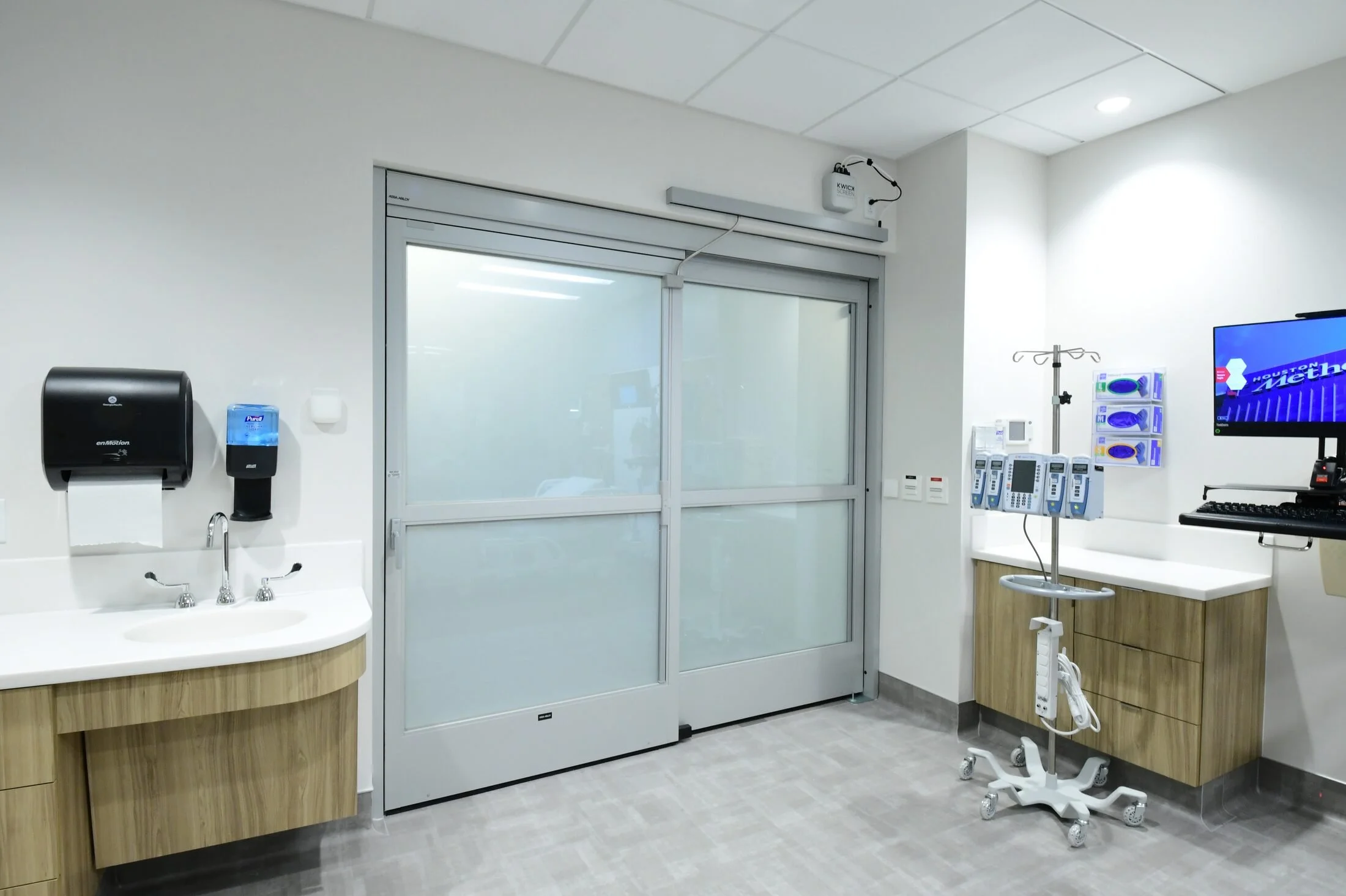 A patient room at Houston Methodist Cypress with its SmartLayer glass door frosted for privacy beside the caregiver workstation.