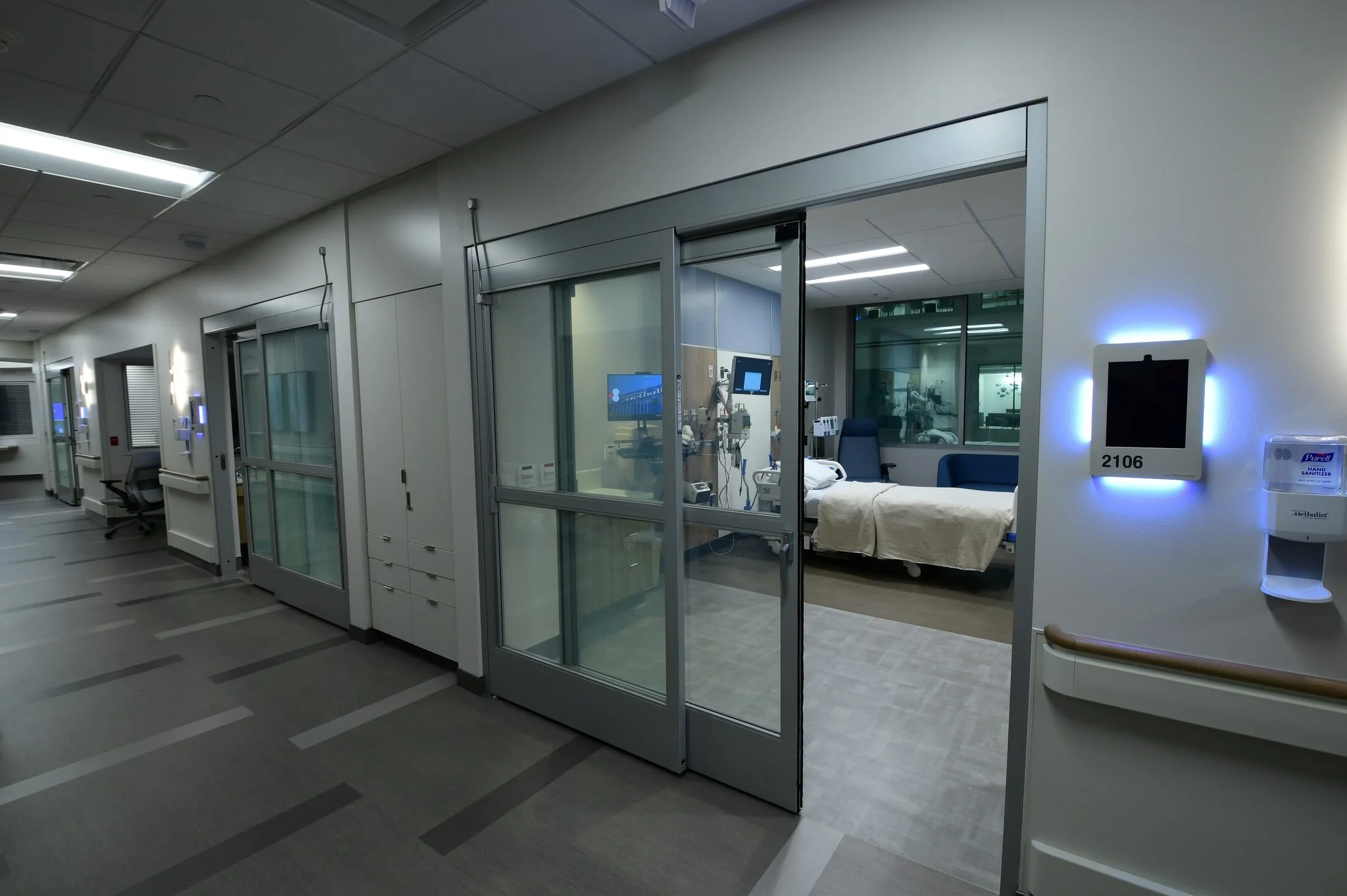 An intensive-care room at Houston Methodist Cypress seen from the corridor, its SmartLayer glass front switched clear to reveal the bed and monitors inside.