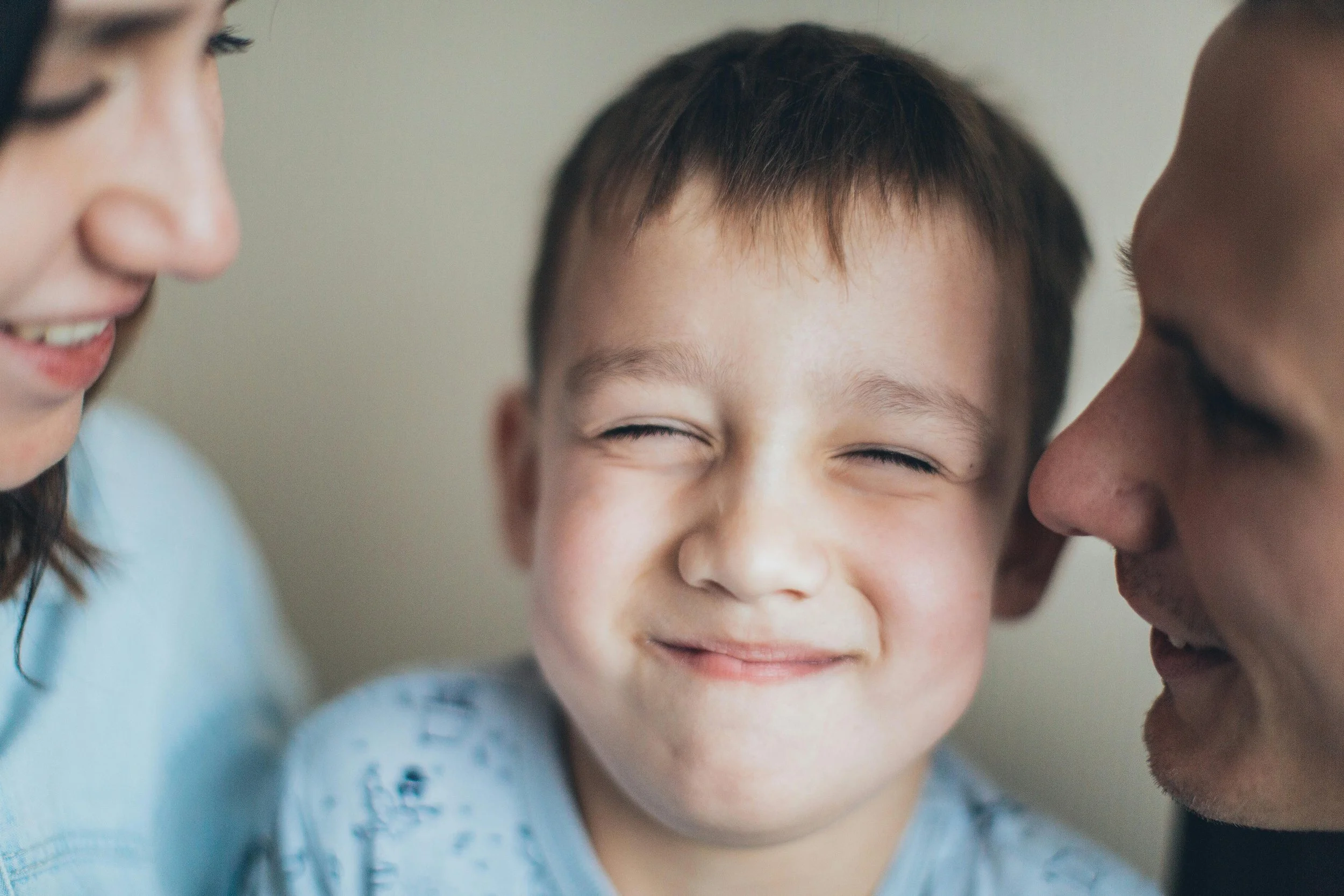 A young boy smiling with eyes closed, flanked by two adults smiling at him.