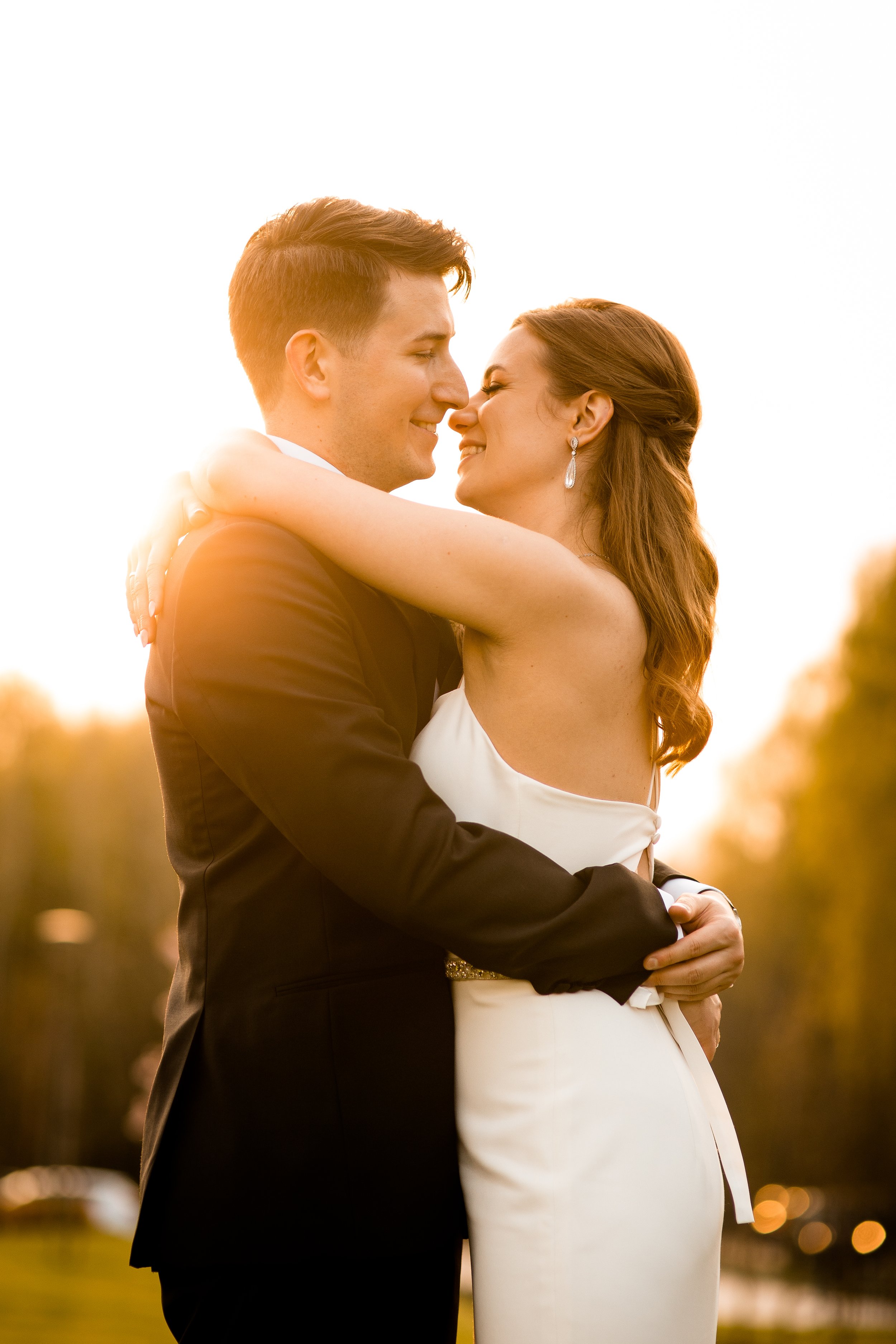 A newlywed couple embracing outdoors during sunset, smiling and looking at each other.