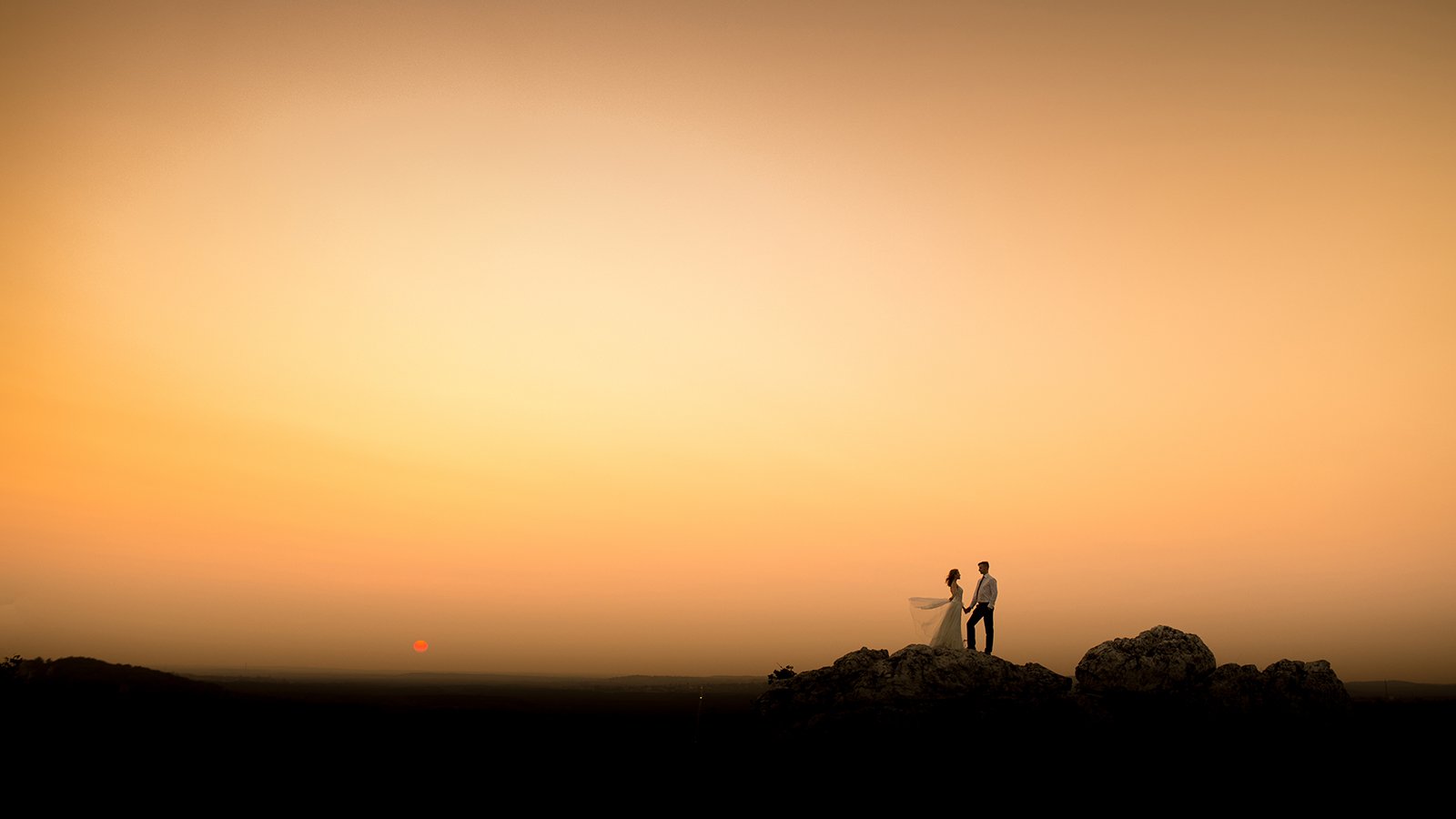 Panna młoda i pan młody trzymają się za ręce i stoją na skałach podczas zachodu słońca.