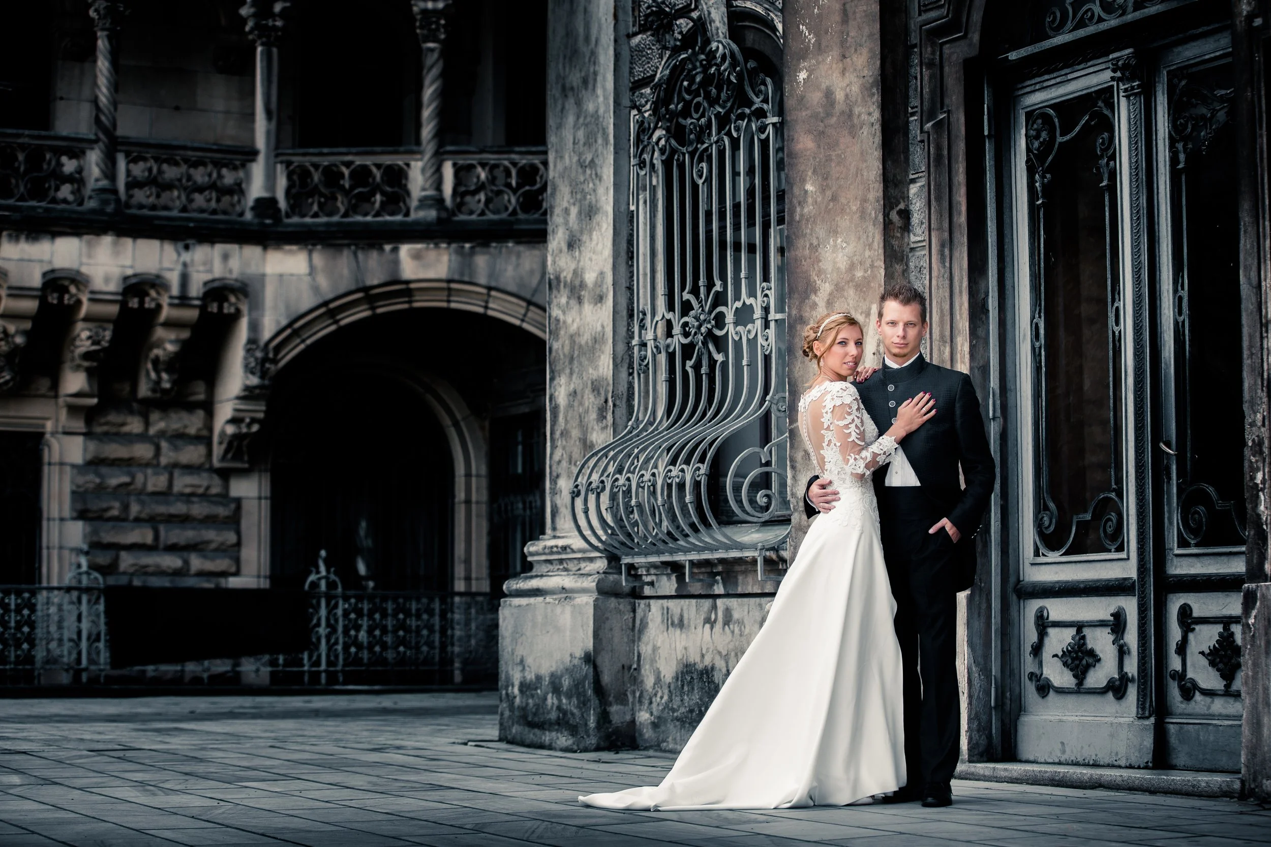 Para młoda stoi blisko siebie przed ozdobną, kutą bramą i zabytkowym budynkiem, na świeżym powietrzu