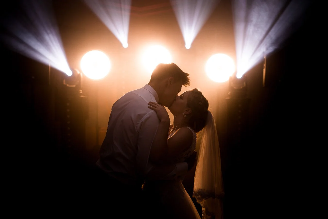 Para całująca się na przyjęciu weselnym z jasnym podświetleniem i reflektorami.