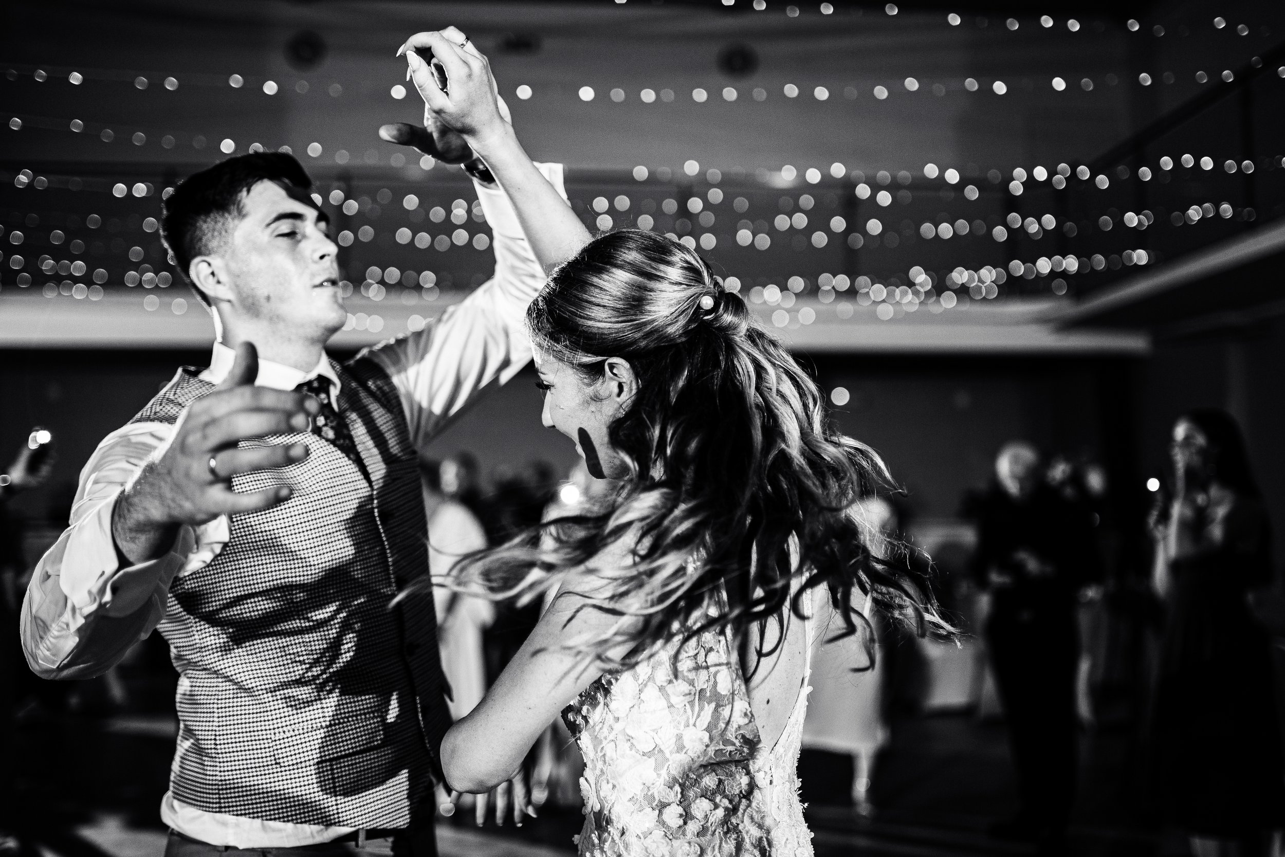 A couple dancing together at a wedding reception, with string lights hanging from the ceiling in the background.