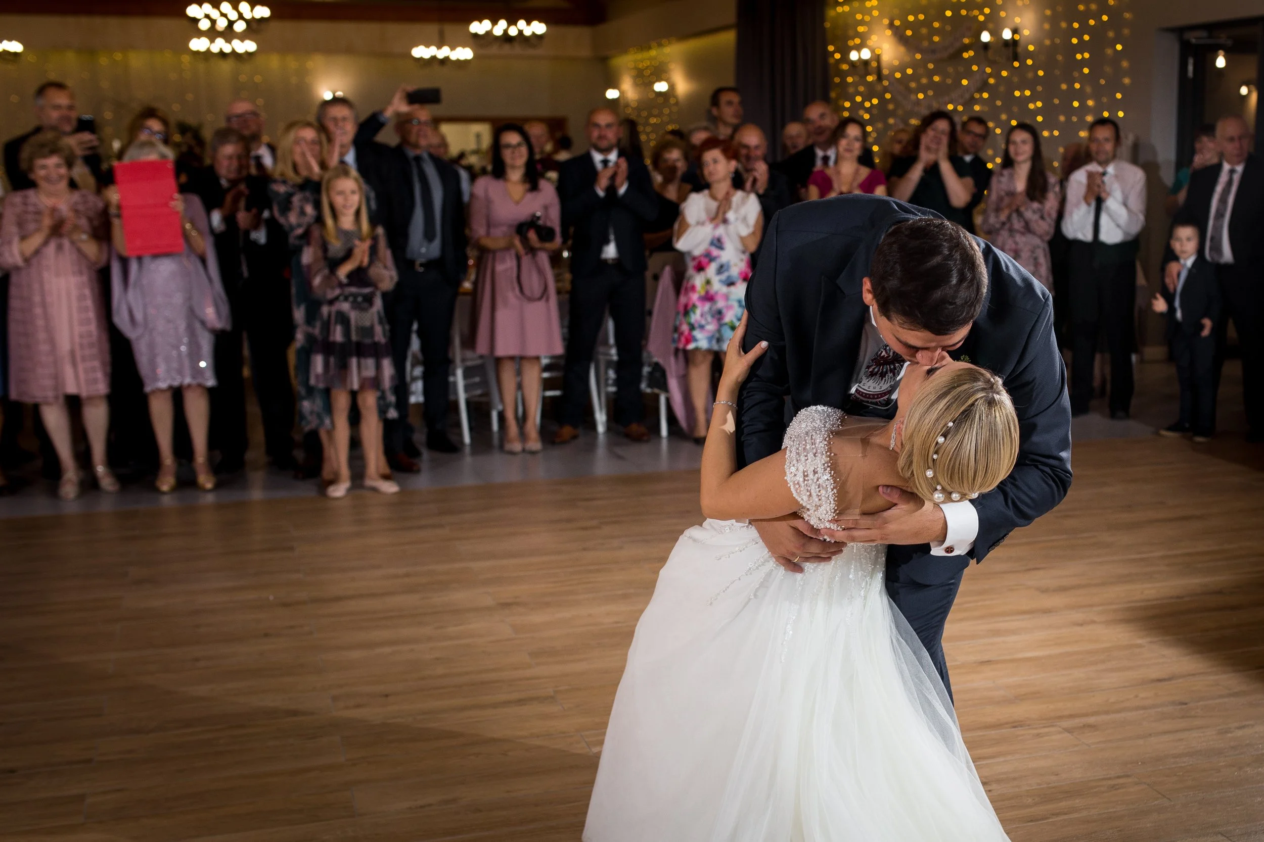 A bride and groom share a dance at their wedding reception, surrounded by guests watching and cheering.