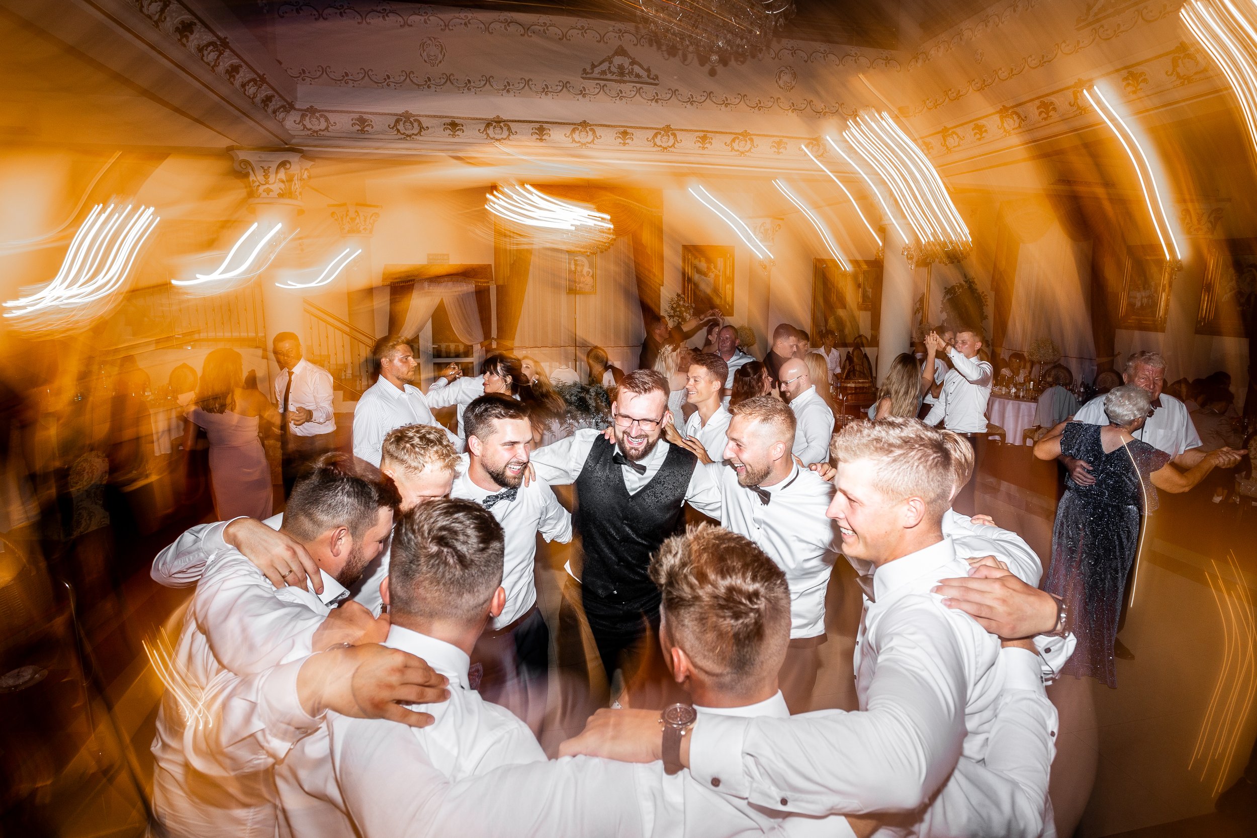 Group of people dancing and celebrating at a wedding reception in a warmly lit, elegant venue.