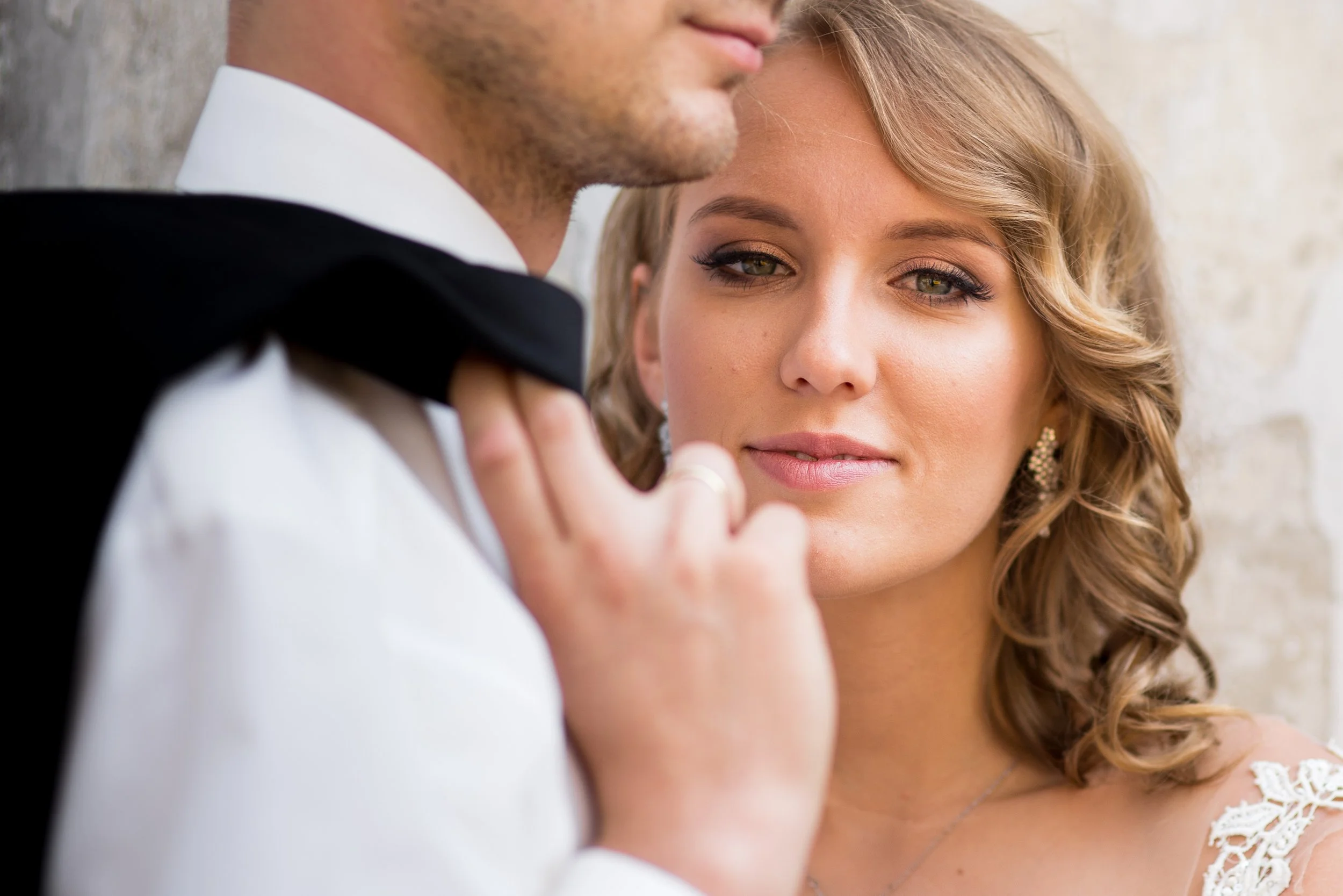 Close-up of a bride and groom, with the bride looking softly at the camera and the groom partially visible, wearing a tuxedo with a bow tie.