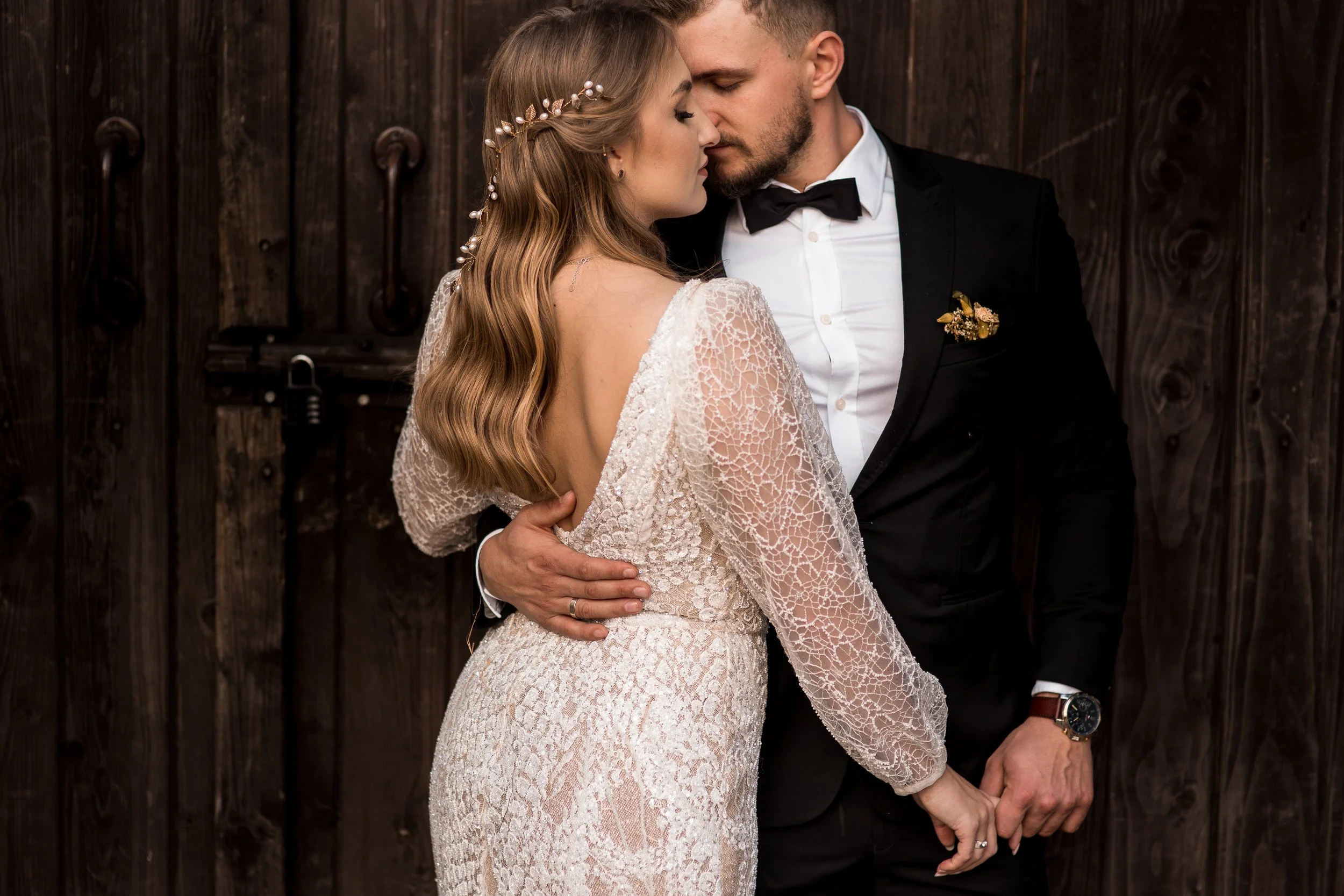 Panna młoda i pan młody przeżywają intymną chwilę, stykając się czołami i mając zamknięte oczy, na tle ciemnego drewna.