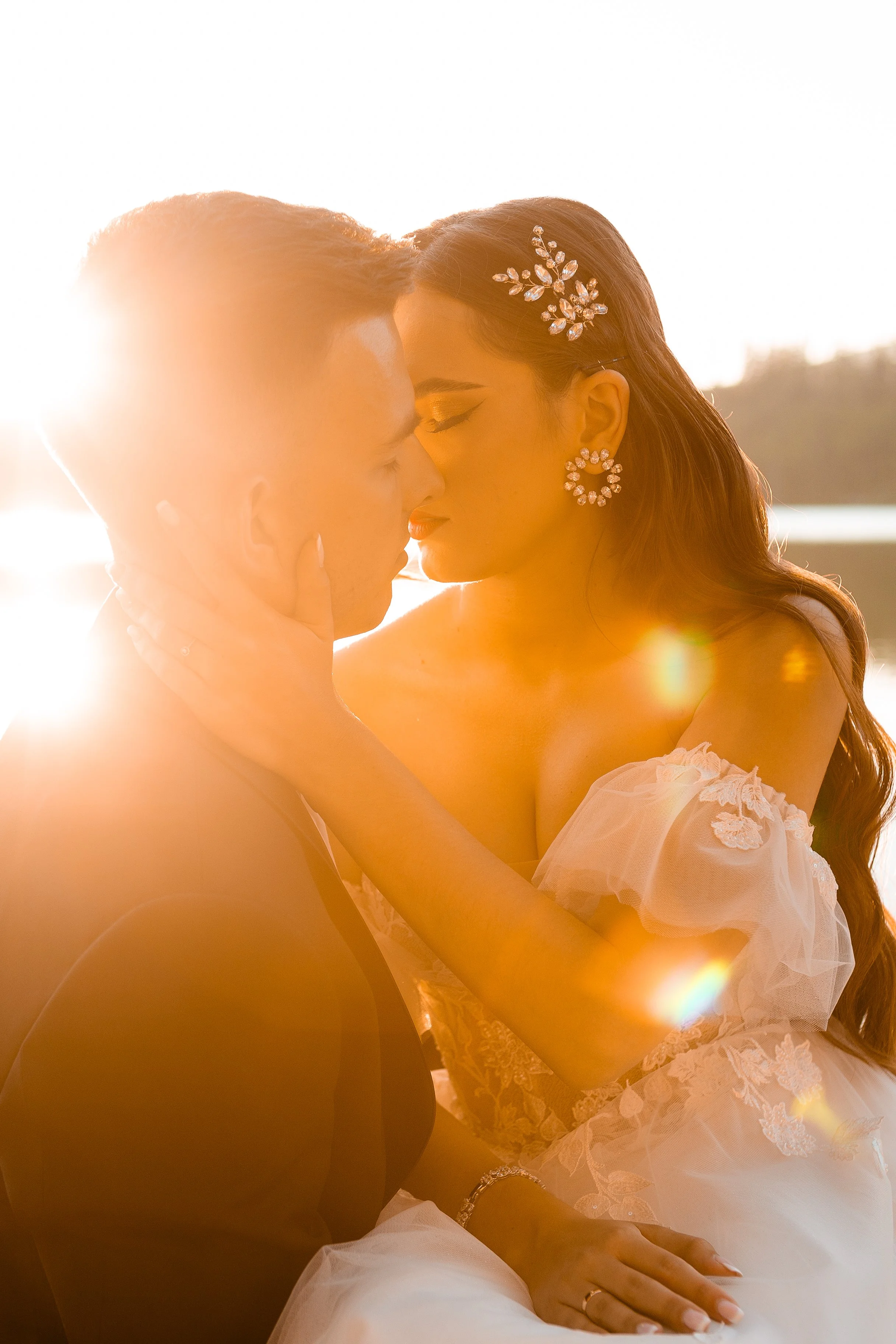 A bride and groom share a romantic kiss during sunset, with the sunlight creating a warm glow around them.