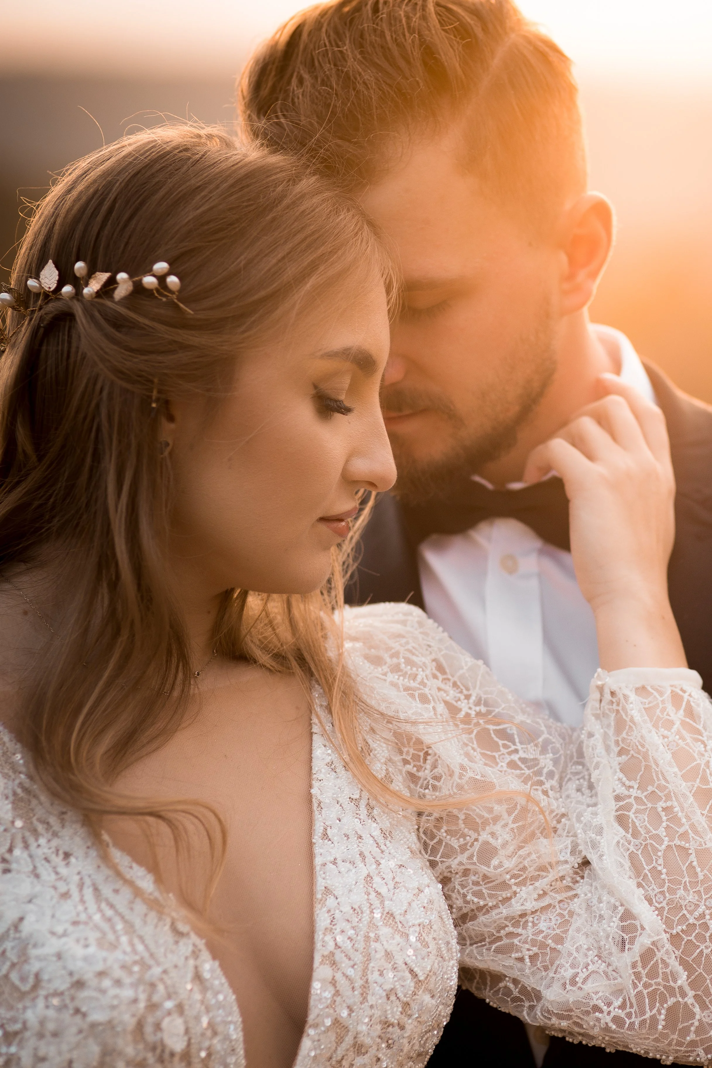 Zbliżenie na pannę młodą i pana młodego w chwili wzruszenia o zachodzie słońca, z zamkniętymi oczami i stykającymi się czołami, ubrani w stroje ślubne.