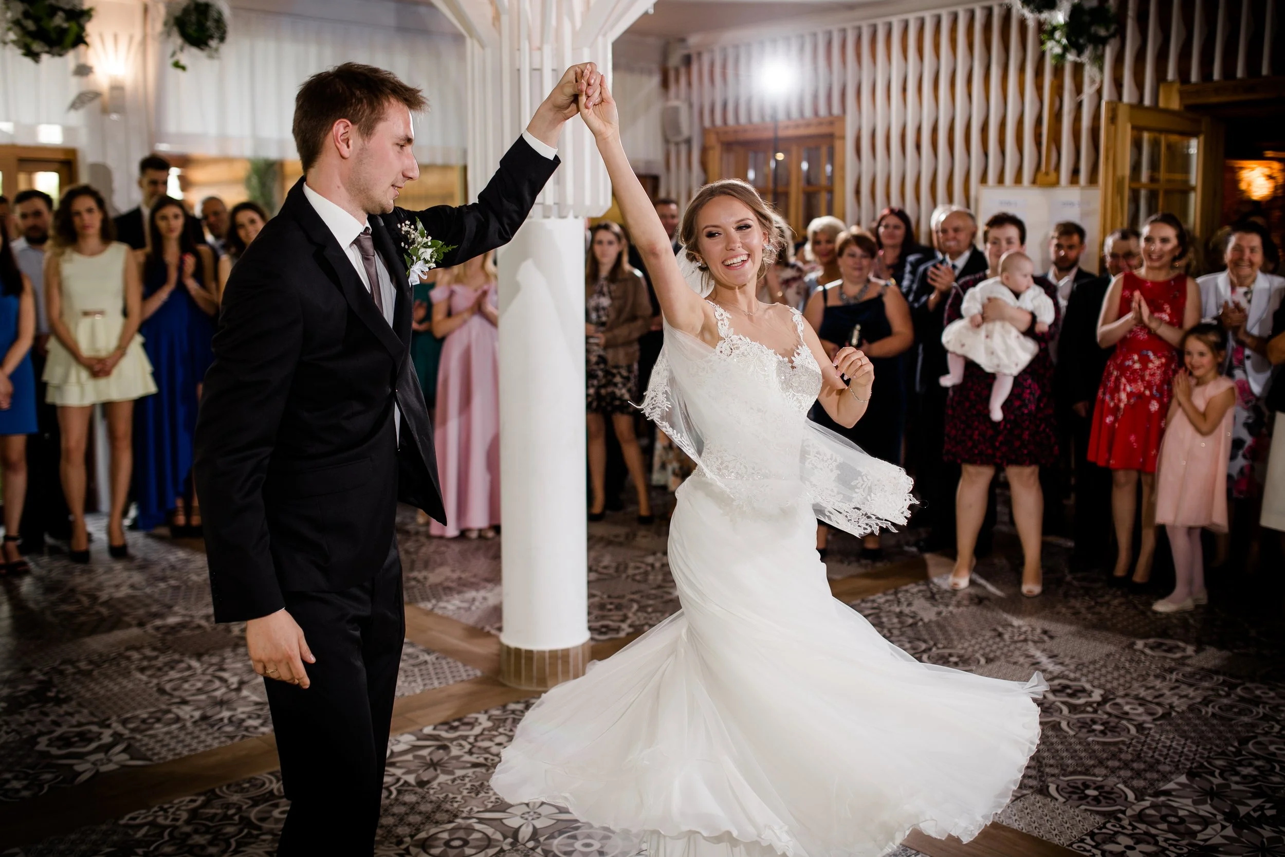 A bride and groom dancing at their wedding reception with guests watching and clapping in the background.