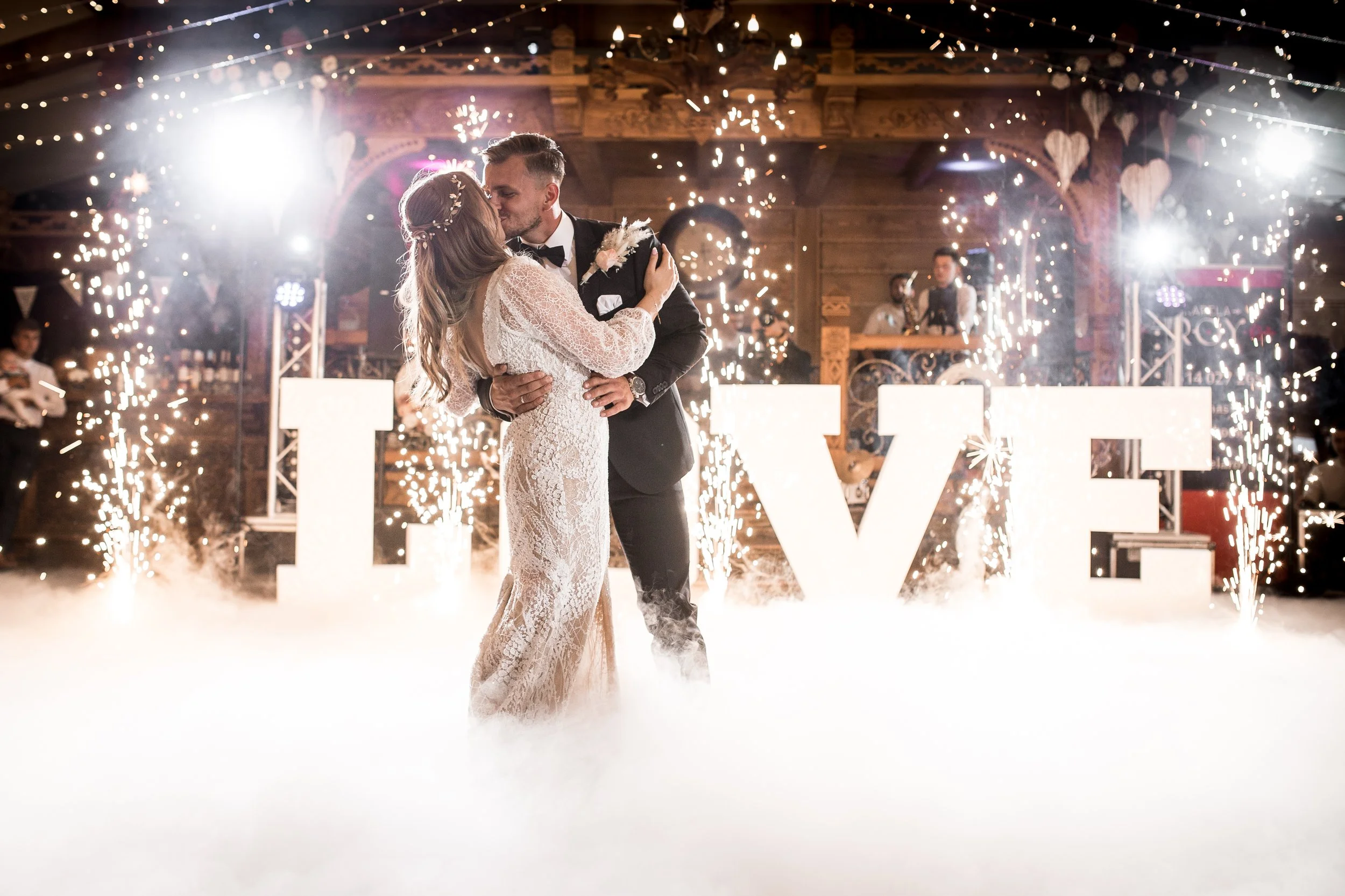 Para młoda wykonująca pierwszy taniec na przyjęciu weselnym, w tle widoczne są zimne ognie i duże, podświetlane listy MIŁOSNE.