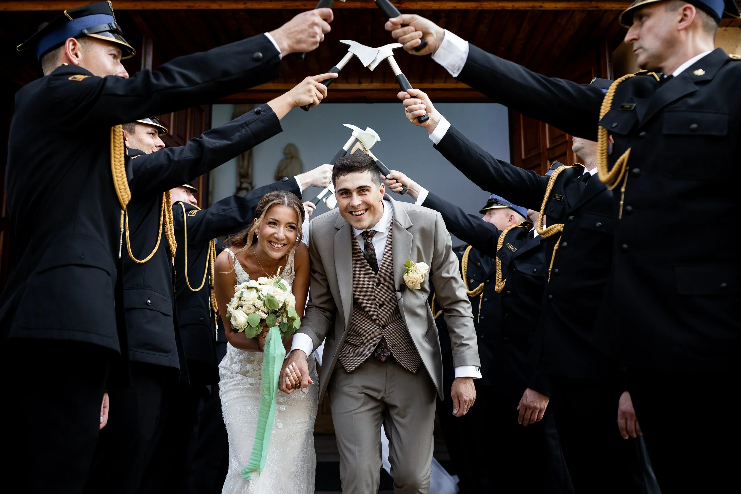 Bride and groom walking through a tunnel of soldiers holding axes over their heads at a wedding celebration.
