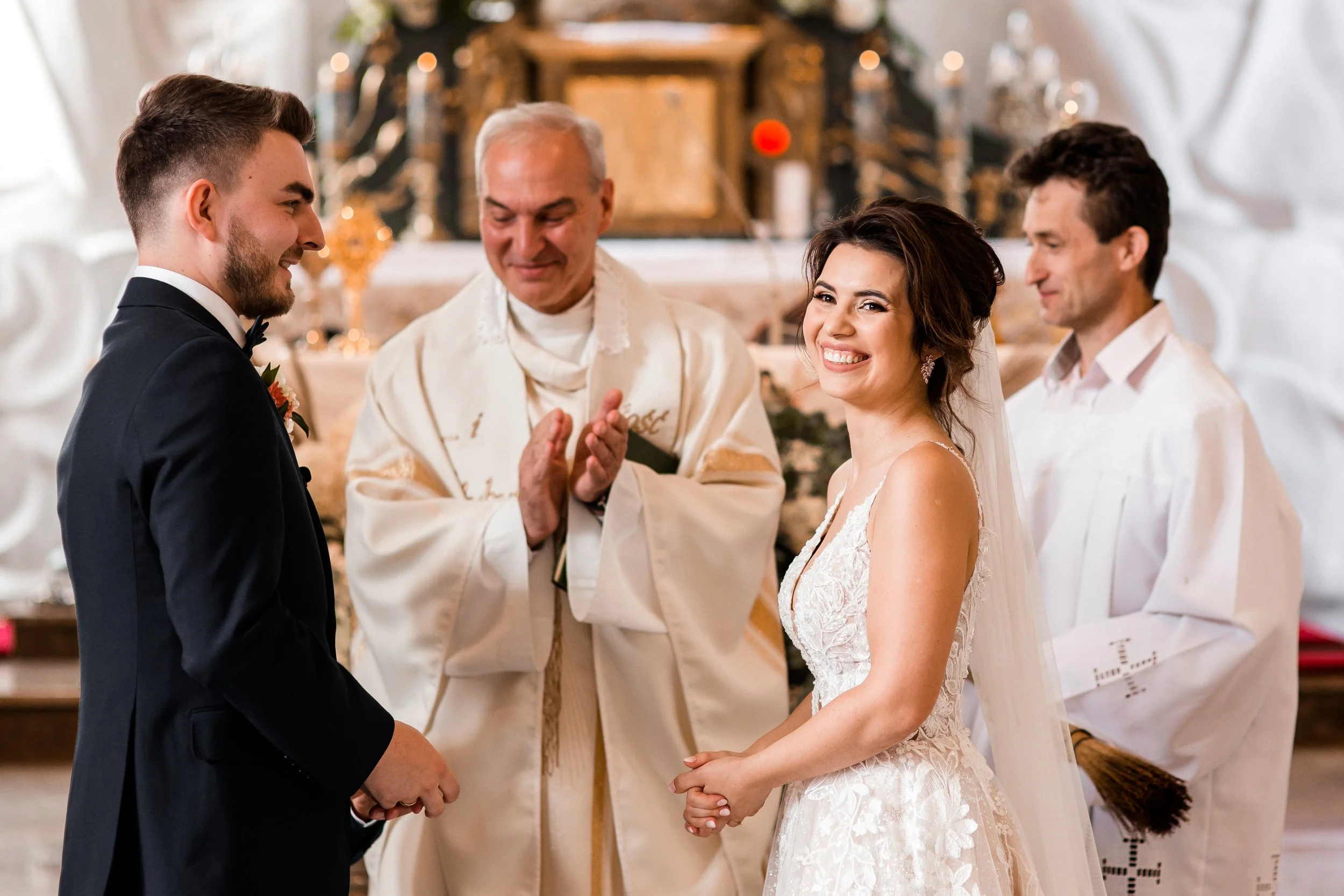 A wedding ceremony with a bride and groom facing each other, surrounded by an officiant and two groomsmen, in a church or chapel with warm decorations.