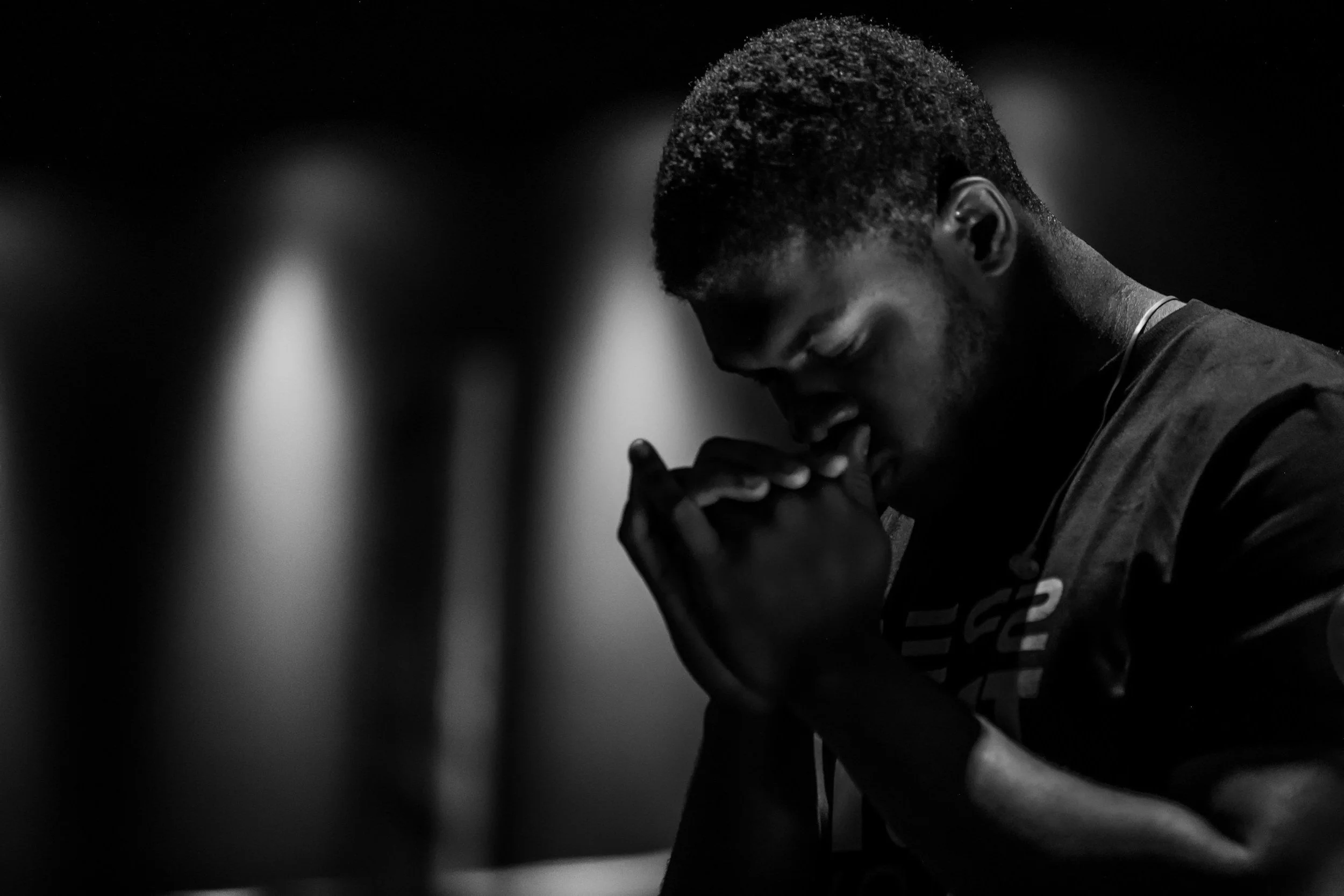 A young man with short hair praying with clasped hands and bowed head in black and white.