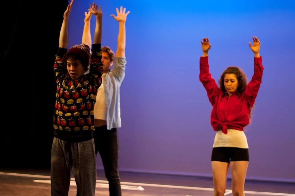 Medium wide shot of EM Williams movement directing and two actors stretch their arms up across a blue purple background