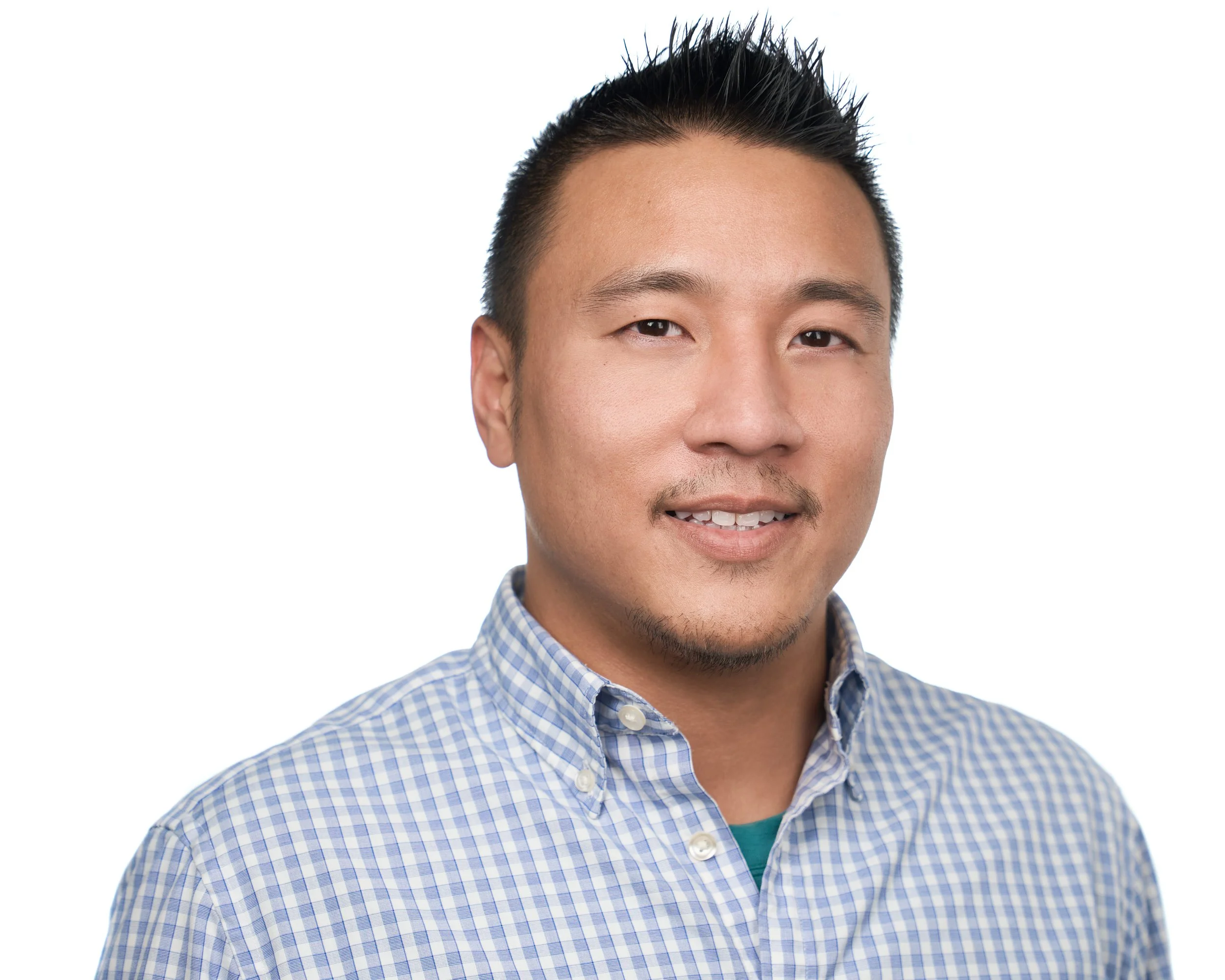 A young Asian man with short, spiked black hair smiling at the camera, wearing a blue and white checkered button-up shirt against a plain white background.