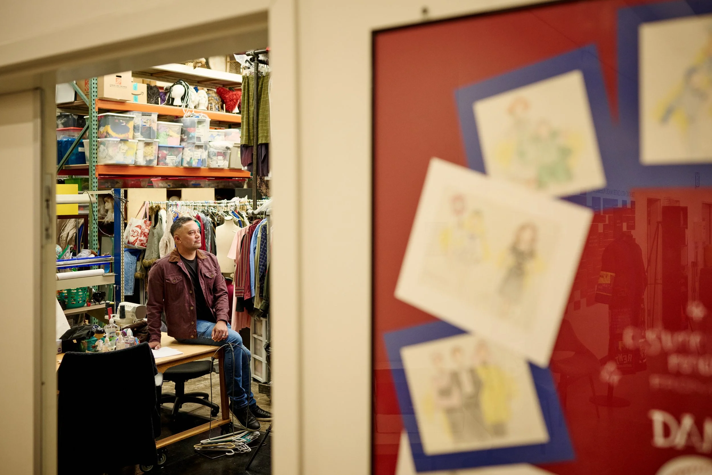 A person sitting behind a desk in a thrift store surrounded by shelves filled with boxes and clothing.