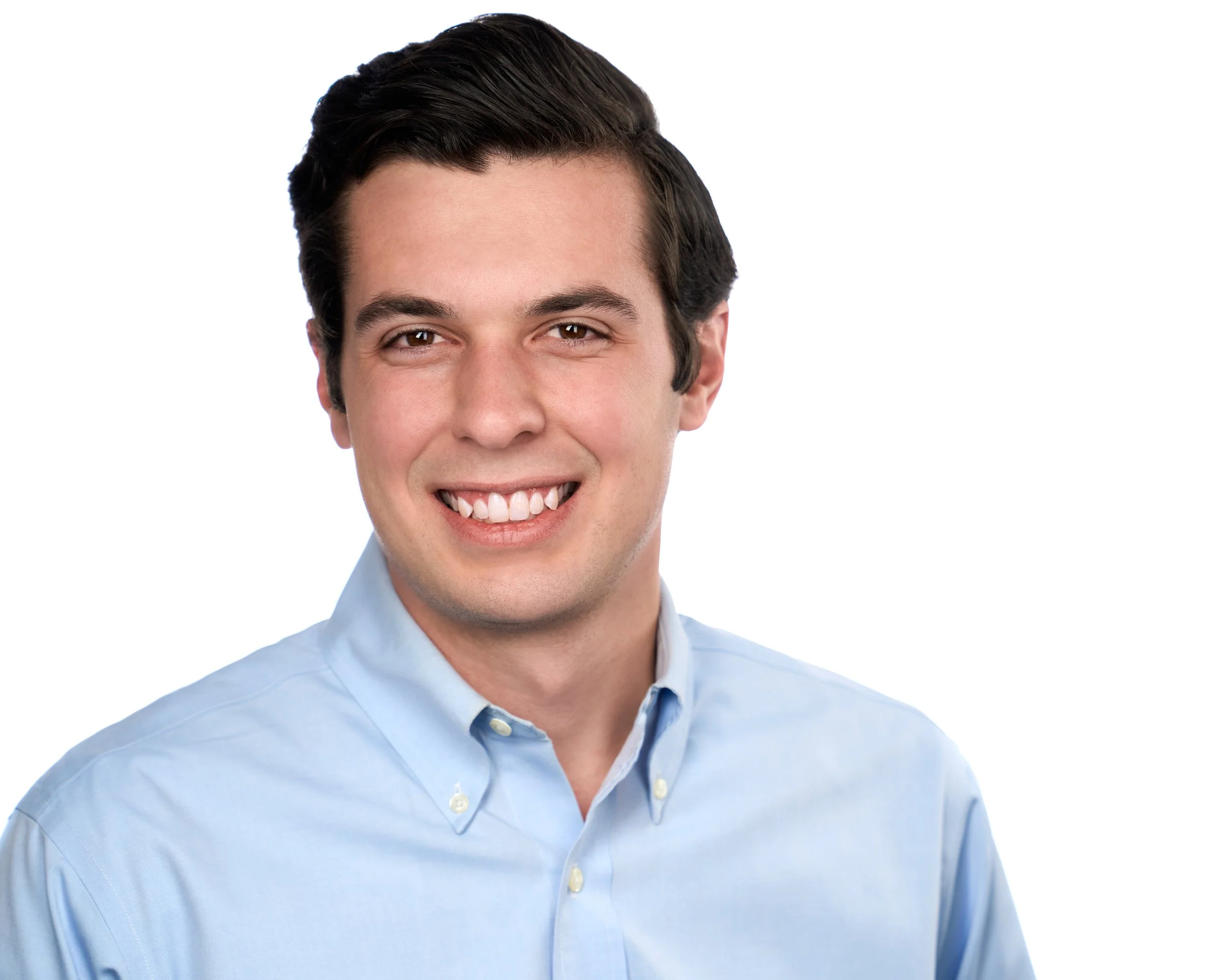 A young man smiling with dark hair, wearing a light blue button-up shirt, against a white background.
