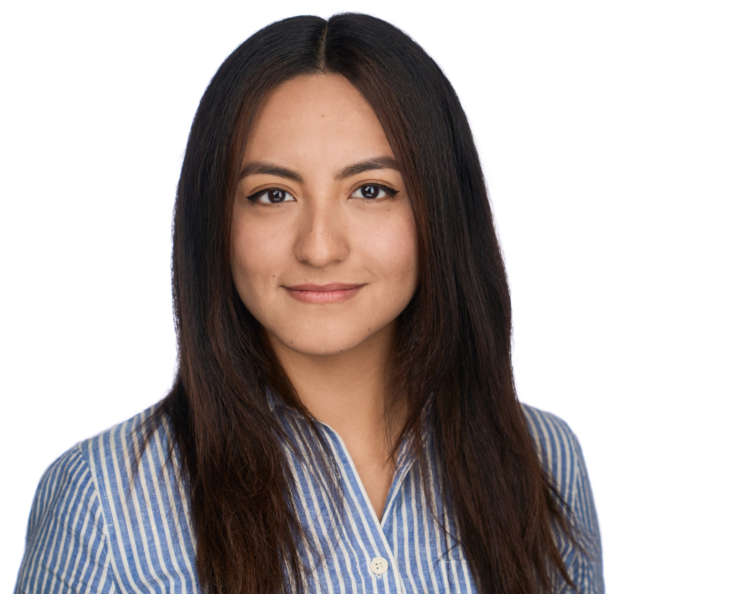 A woman with long dark hair, light skin, wearing a blue and white striped shirt, smiling, against a plain white background.