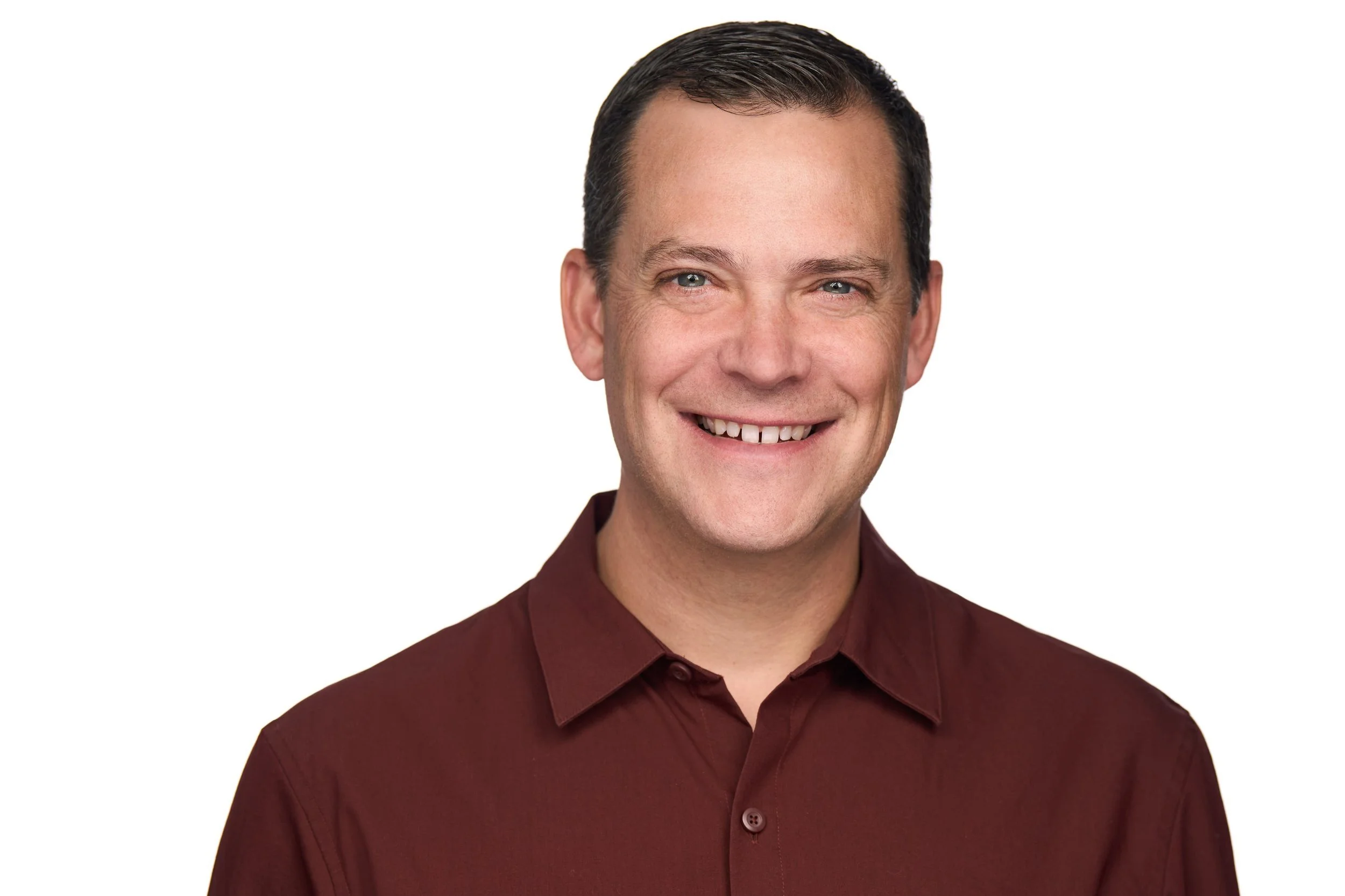 Headshot of a smiling man with short dark hair wearing a maroon button-up shirt against a white background.