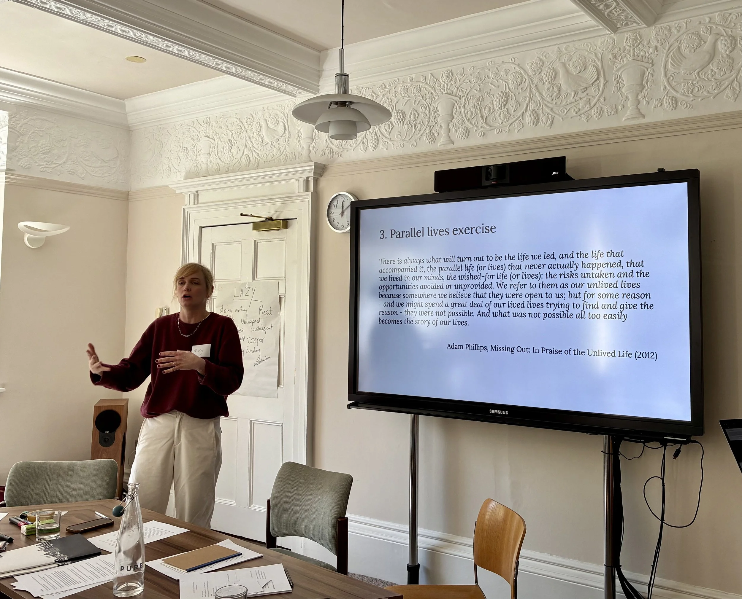 Workshop facilitator Nicolas Sayers explaining the activity to the workshop participants with a presentation slide in the background titled Parallel lives exercise and a quote from Adam Phillips' book Missing Out: In Praise of the Unlived Life (2012)