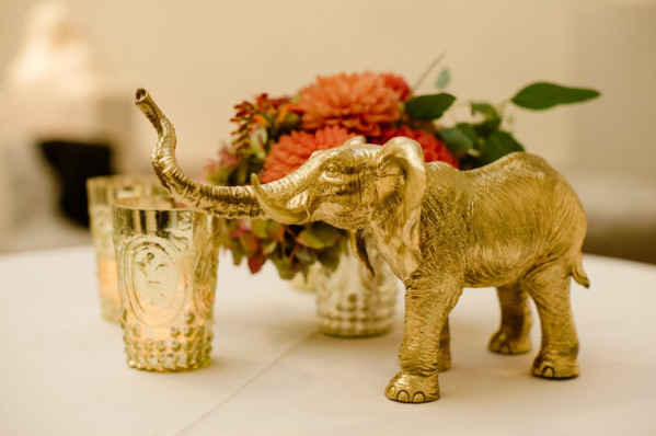 Table decor with a golden elephant figurine, a small bouquet of red flowers, and gold-textured votive candle holders.