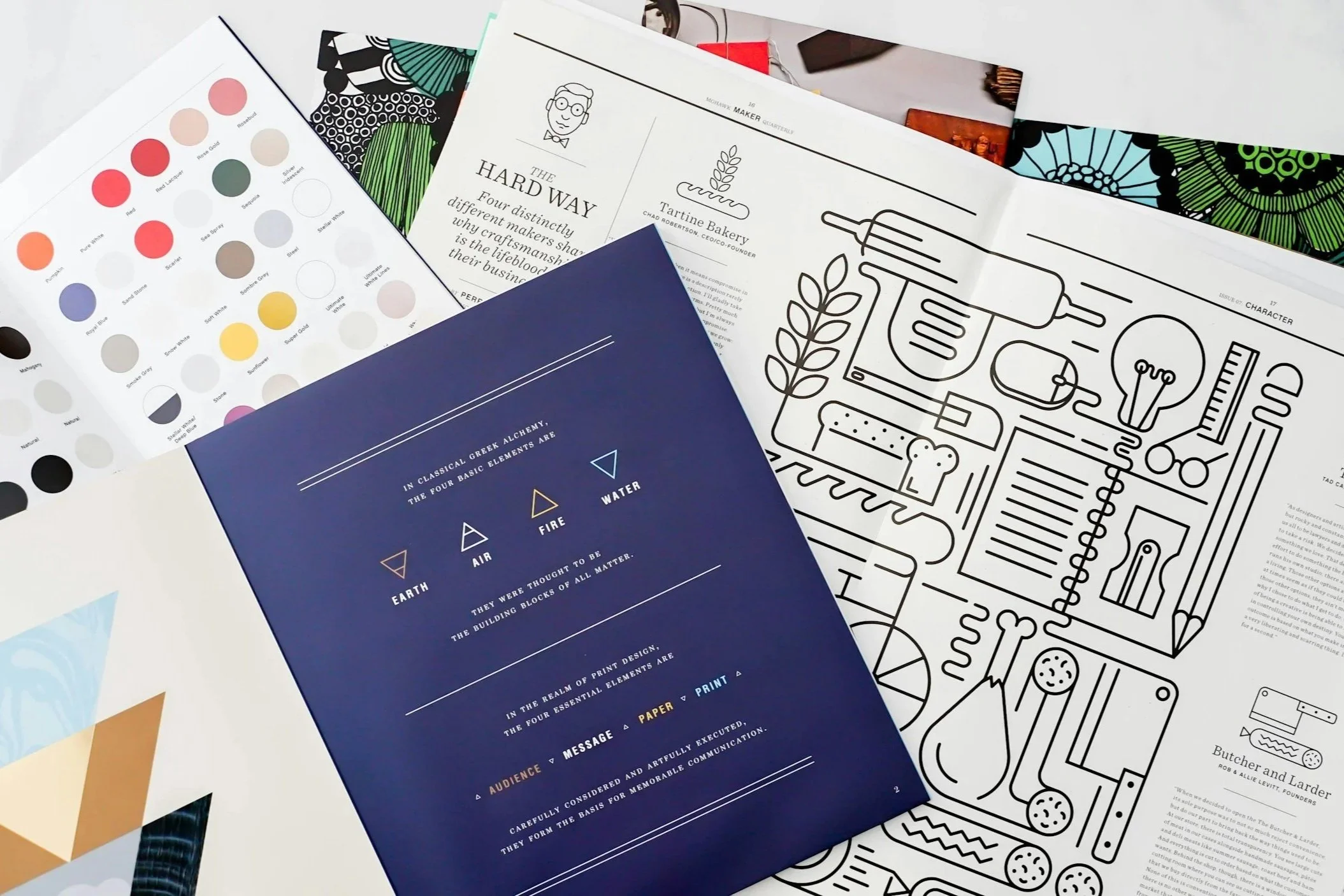 A collection of printed pages and pamphlets, including a color palette, a blueprint-like infographic about the four elements, and outlines of a bakery and butchery business.