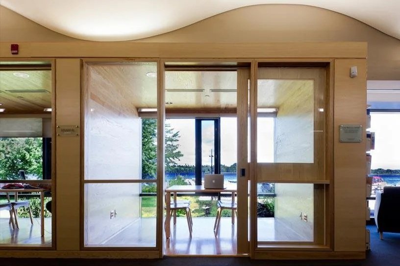 Office space with a wooden waiting area, glass walls, and a view of trees and a body of water outside.