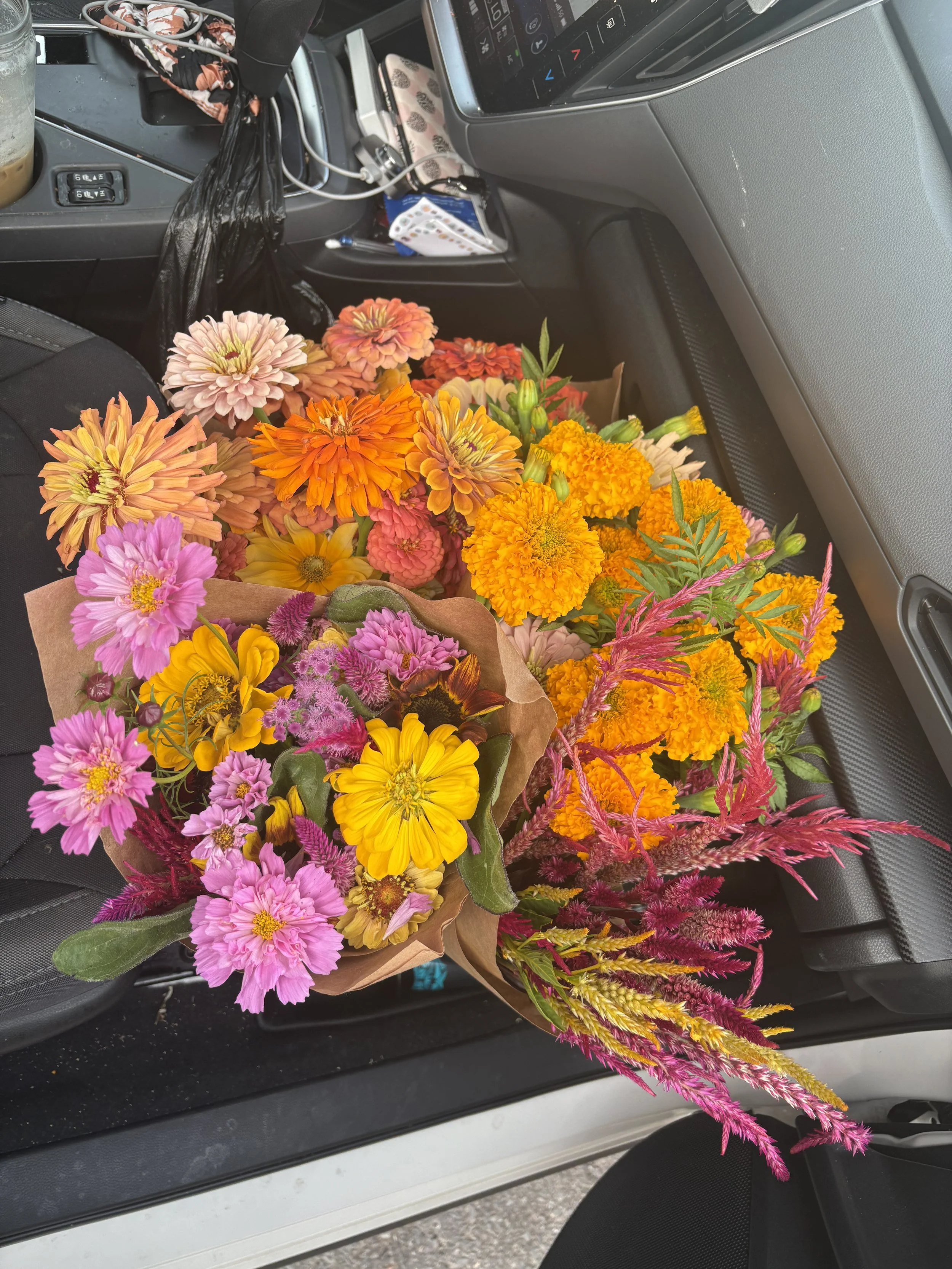 Bright mixed bouquet of pink, yellow, orange, and purple flowers resting on a car seat.