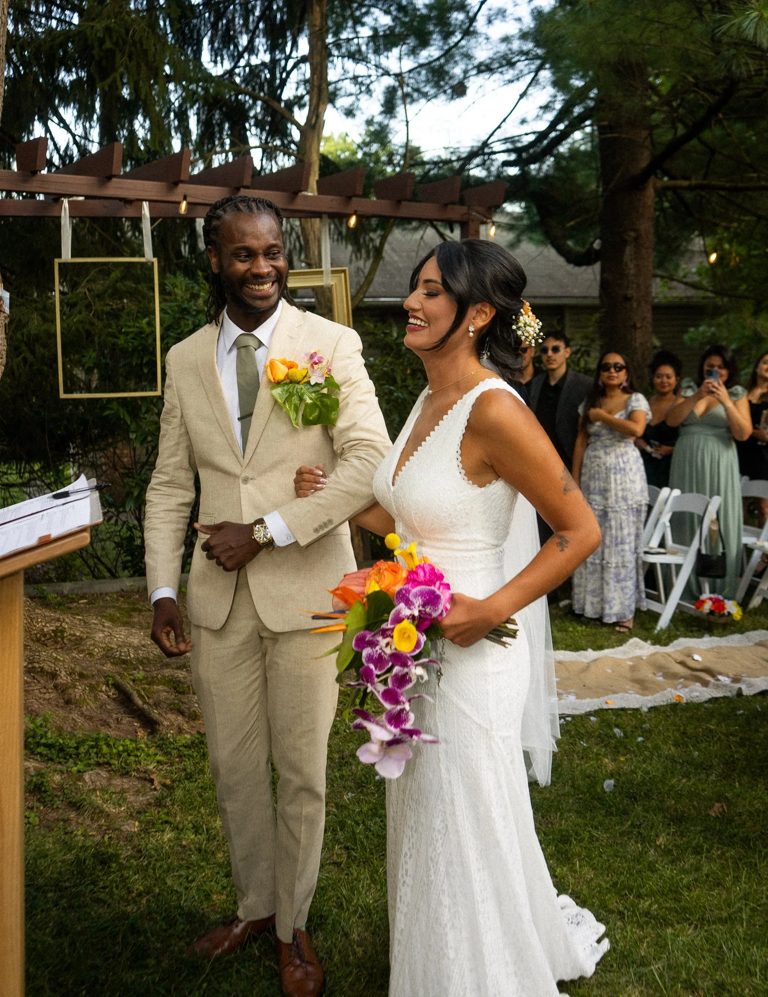 A bride and groom exchanging vows during their outdoor wedding ceremony, with guests watching in the background.