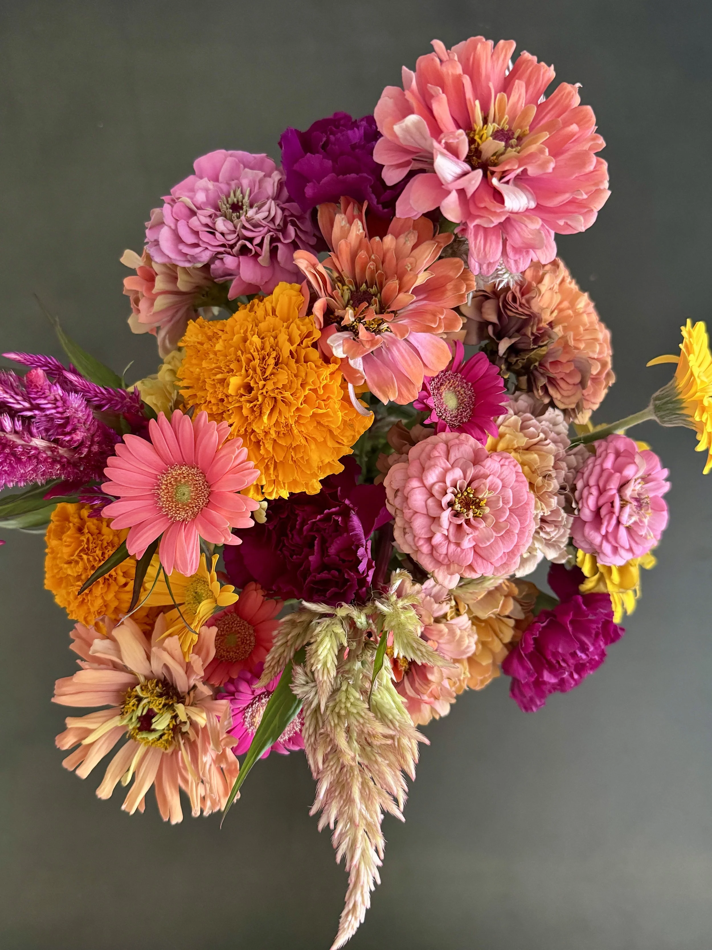 Colorful bouquet of various pink, orange, purple, and yellow flowers against a dark background.