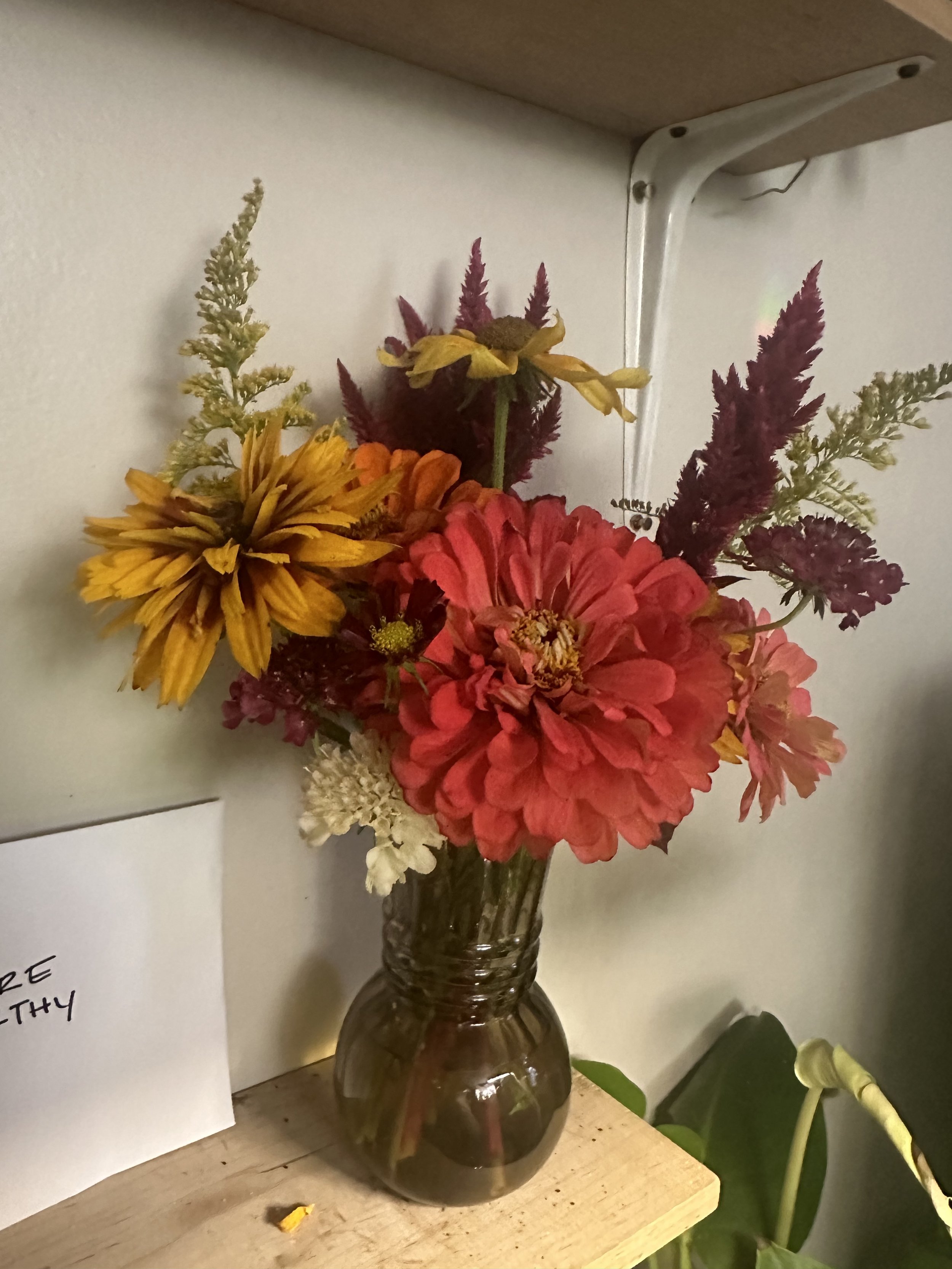 Colorful flower bouquet in a small glass vase on a wooden surface.