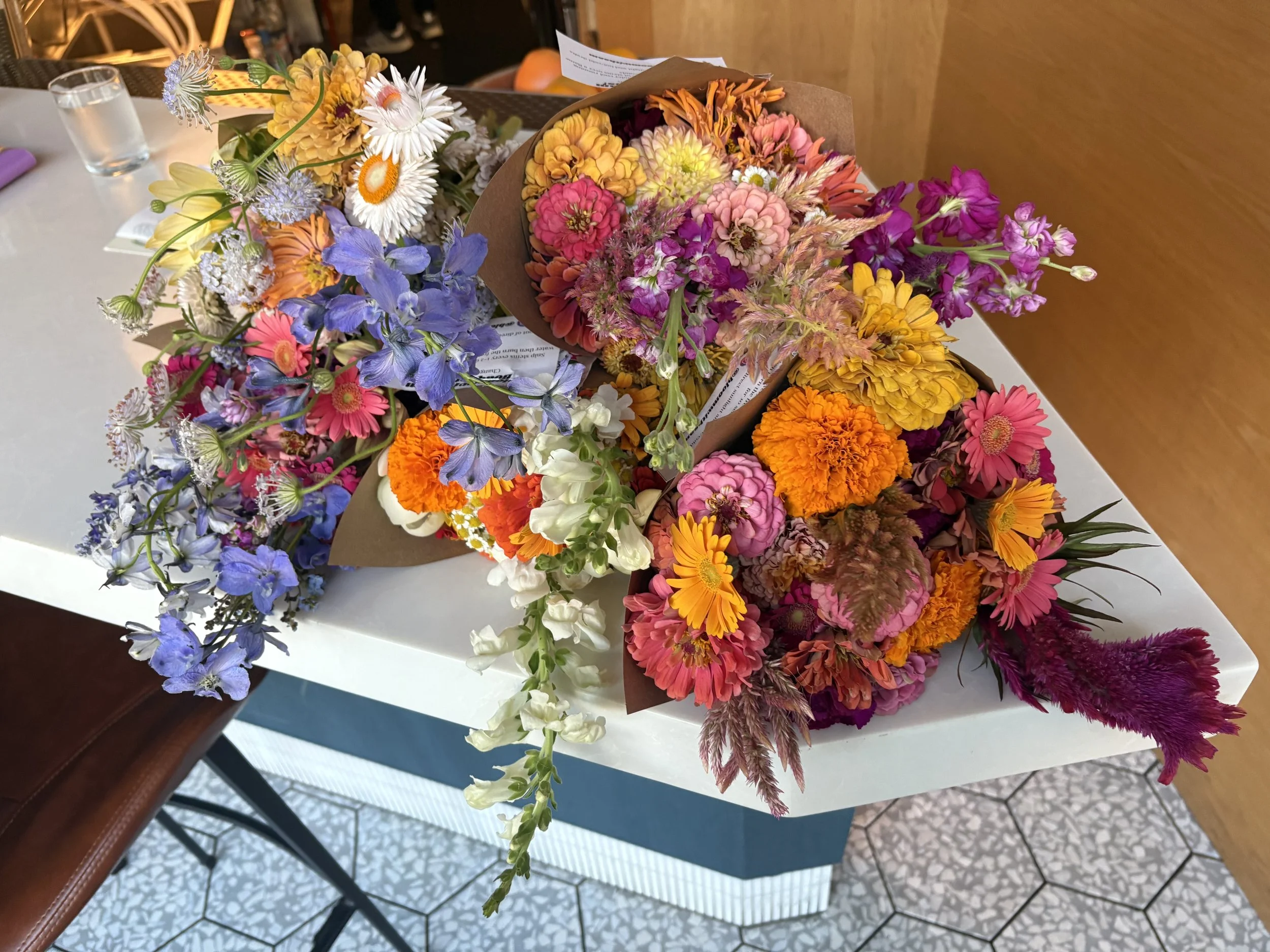 Multiple colorful flower bouquets on a table, including orange, pink, purple, white, and yellow flowers.