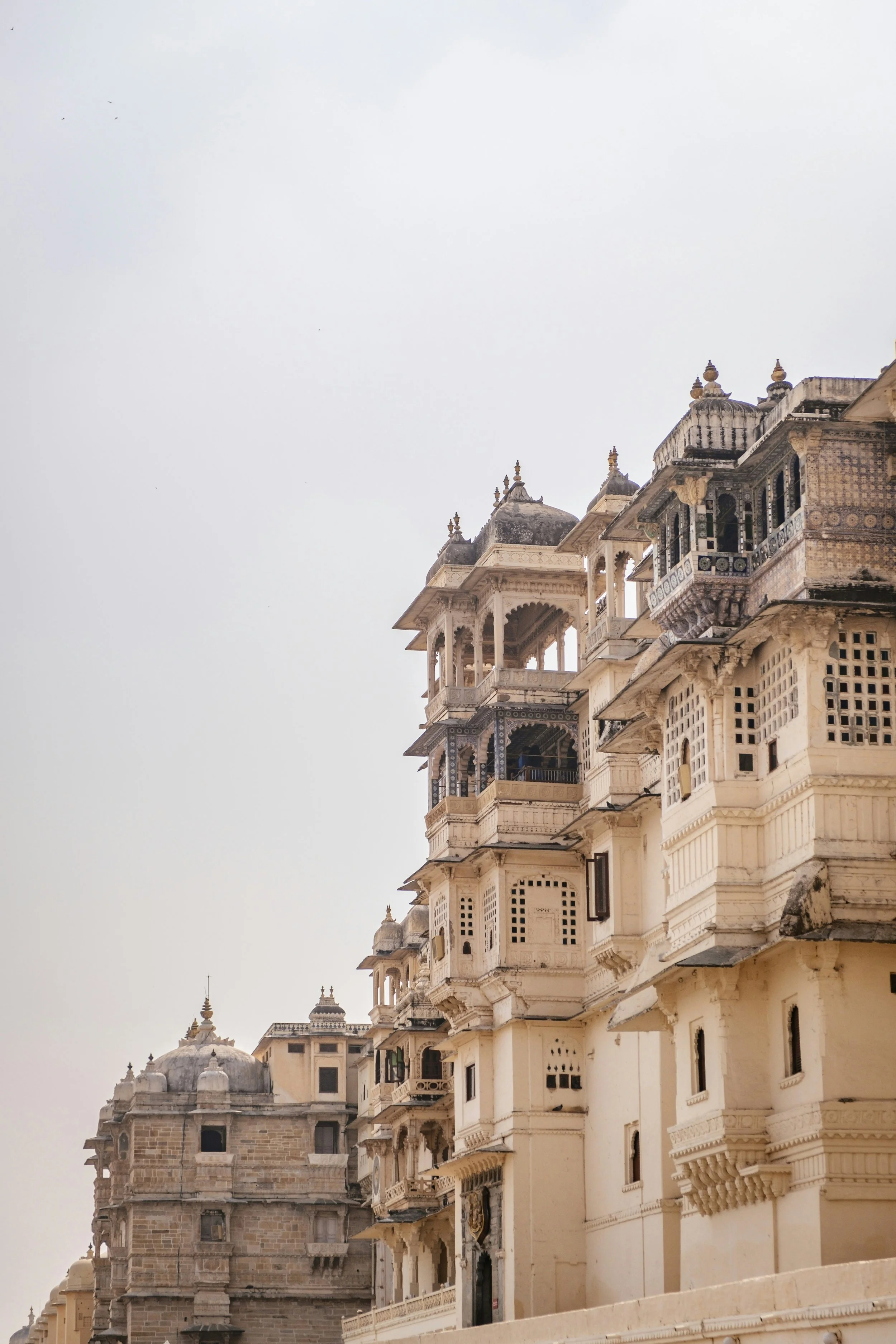 Historical stone and white-painted building with intricate architectural details and multiple balconies, likely part of a palace or fort, on a cloudy day.