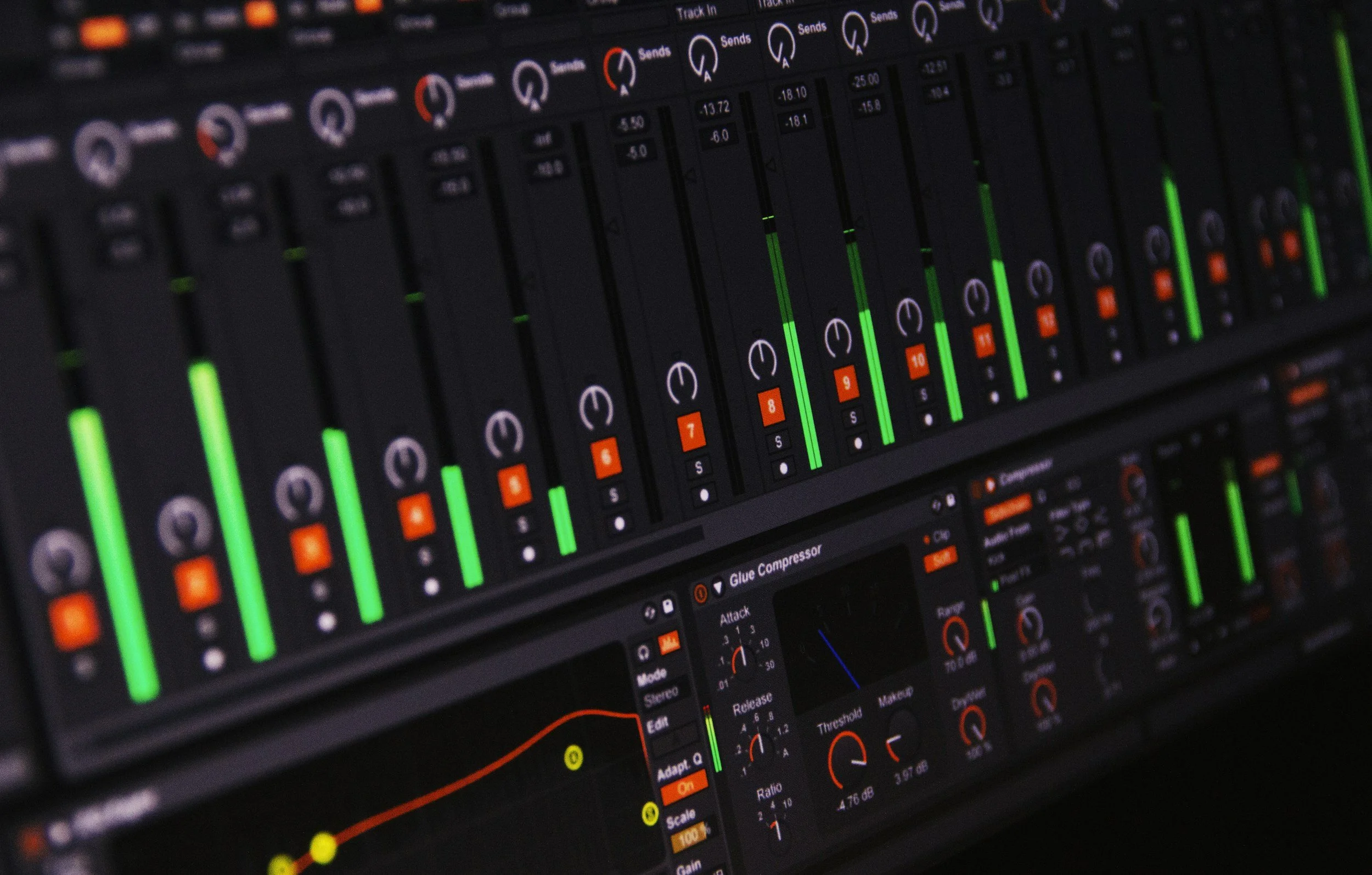 Close-up of a digital audio mixing console with multiple sliders, knobs, and LED indicators in green and orange.