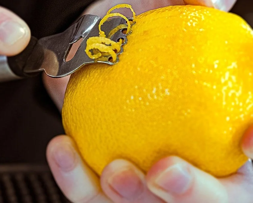 Person peeling a large yellow lemon with a vegetable peeler.