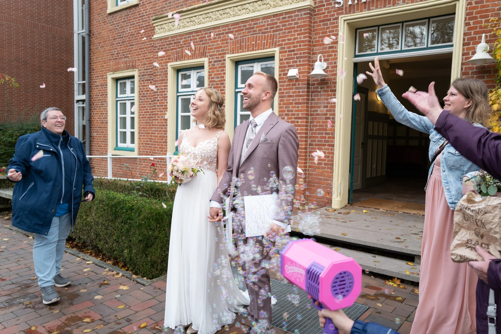 Ein Brautpaar wird beim Hochzeitsschießen mit einer Seifenblasenkanone von Freunden begrüßt.