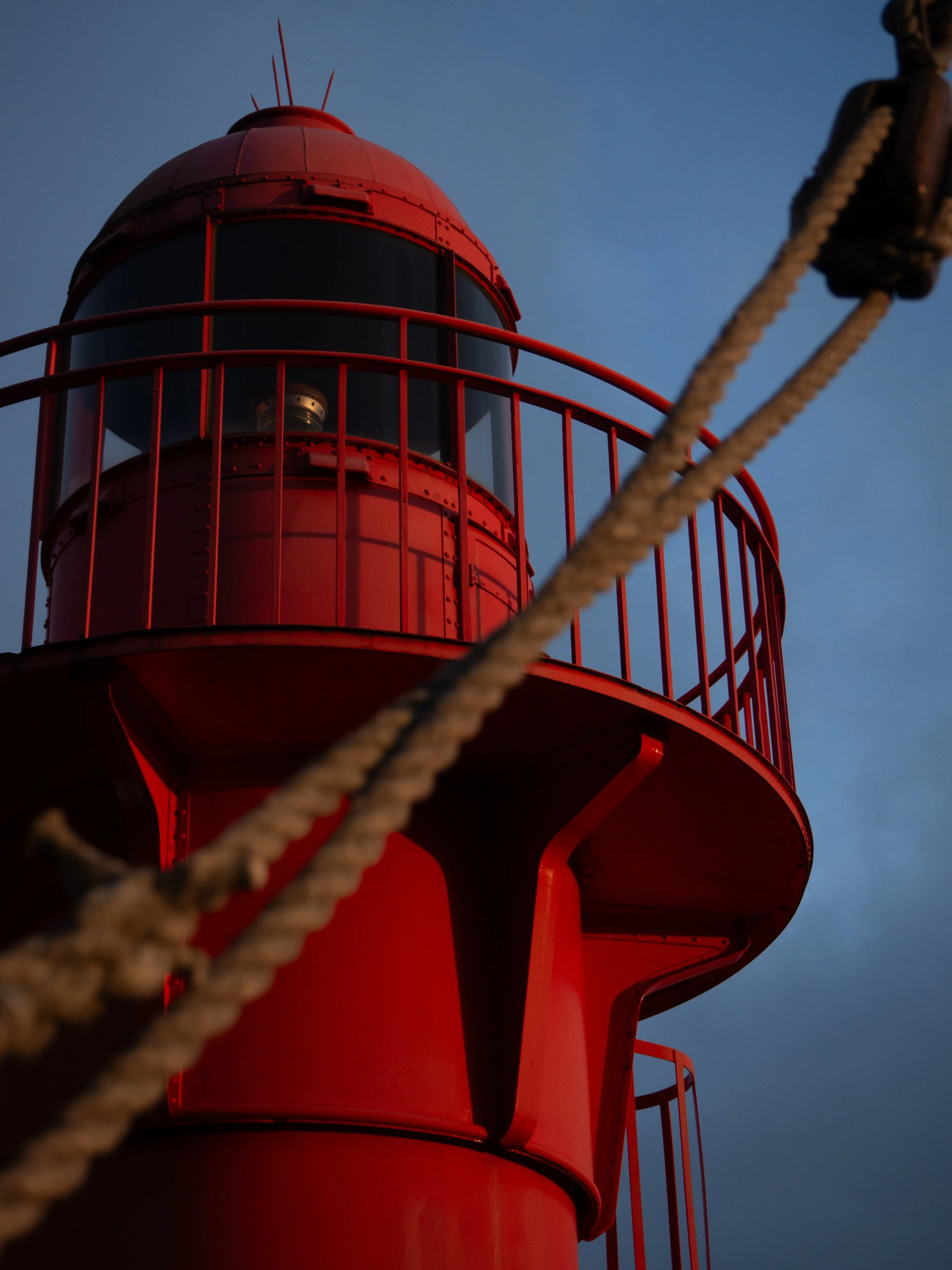 Roter Leuchtturm mit Seil im Vordergrund bei Sonnenuntergang.