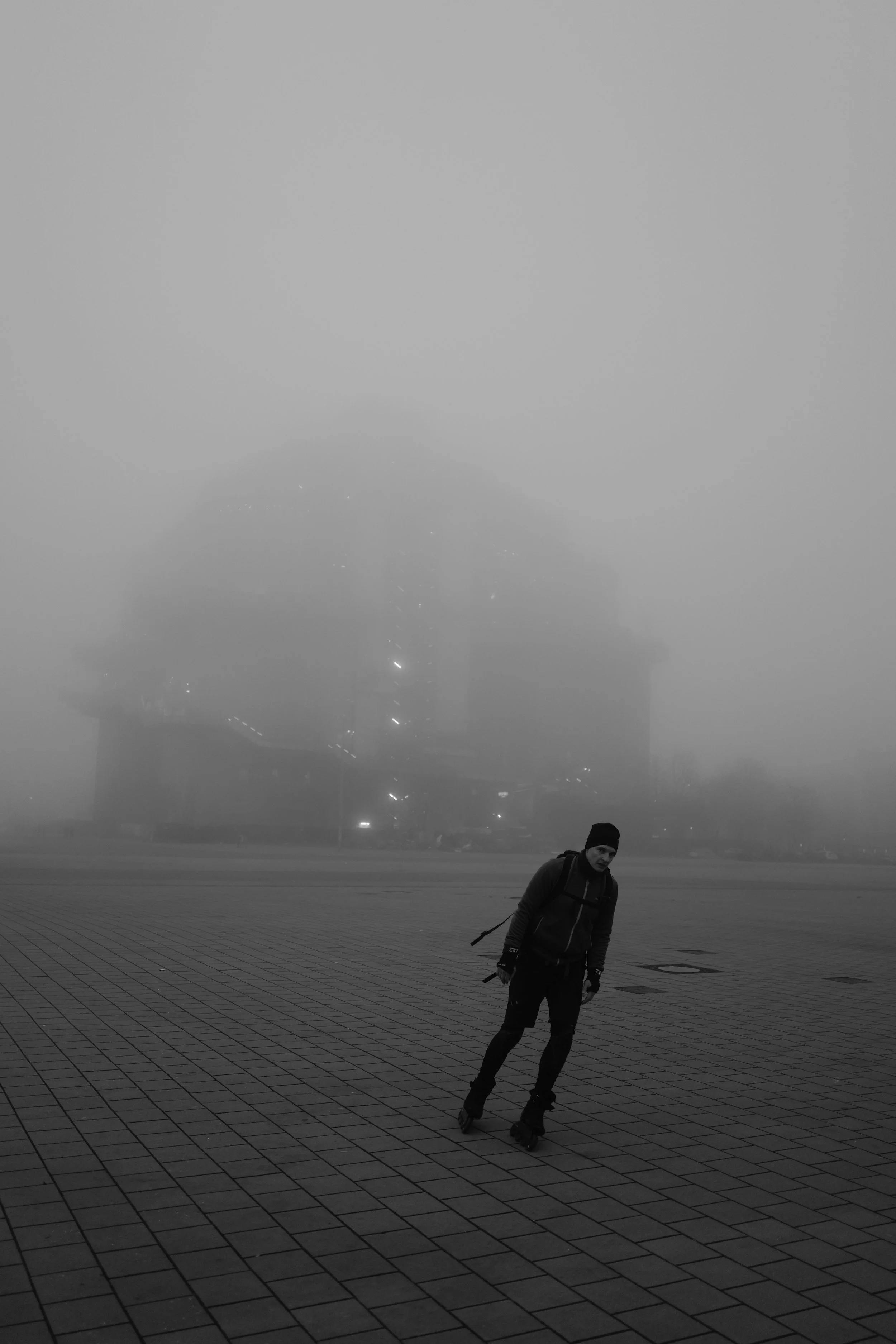 Eine Person in Inlineskates auf einem nebligen Platz mit einem unscharfen Gebäude im Hintergrund.